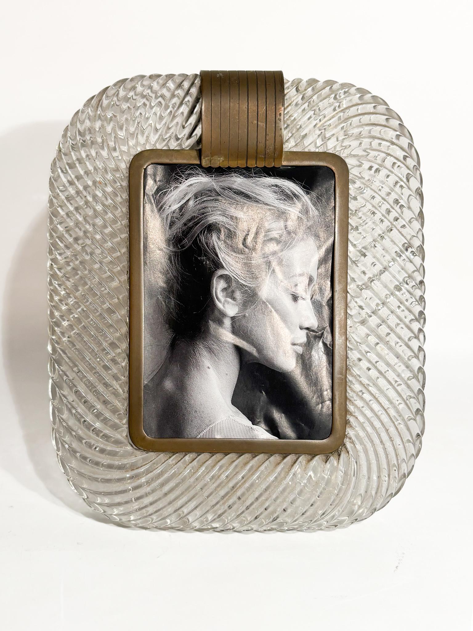 Cadre photo en verre blanc de Murano et laiton, attribué à Venini dans les années 1940

Ø cm 19 Ø cm 2,5 h cm 22

Venini est un nom qui évoque immédiatement l'excellence et le raffinement du verre de Murano. Cette verrerie vénitienne historique,