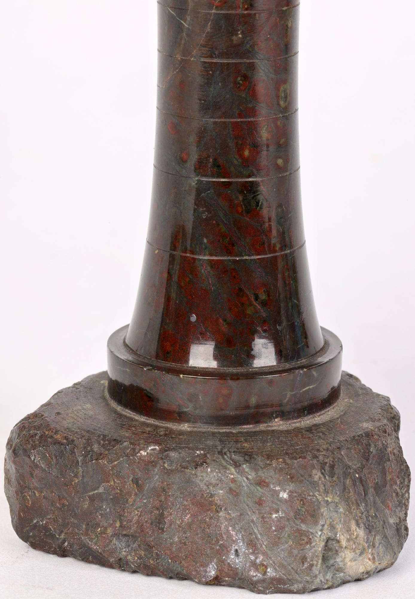 A stylish Cornish carved red serpentine stone ware model of a lighthouse dating from the early to mid 20th Century. The lighthouse is carved from a single piece of stone with the base left unpolished in its natural state to give the effect of the