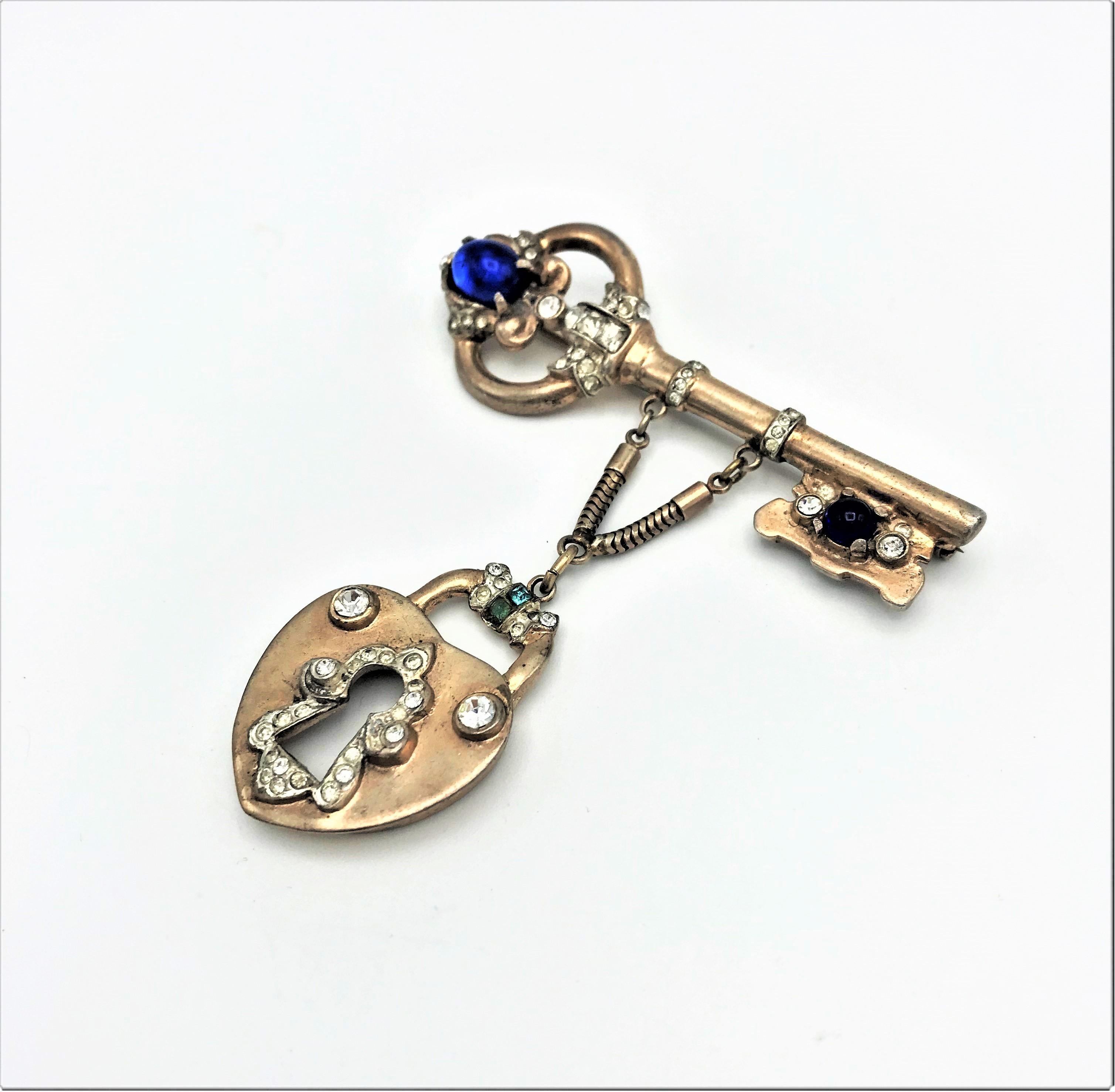 A key-shaped brooch with an attached lock designed by Coro Craft in the 1940s in sterling gold plated.  Decorated with blue rhinestones and small clear rhinestones.
Measurement: Key wide 7 cm x 2,5 cm, the full length with the lock 8 cm . Good