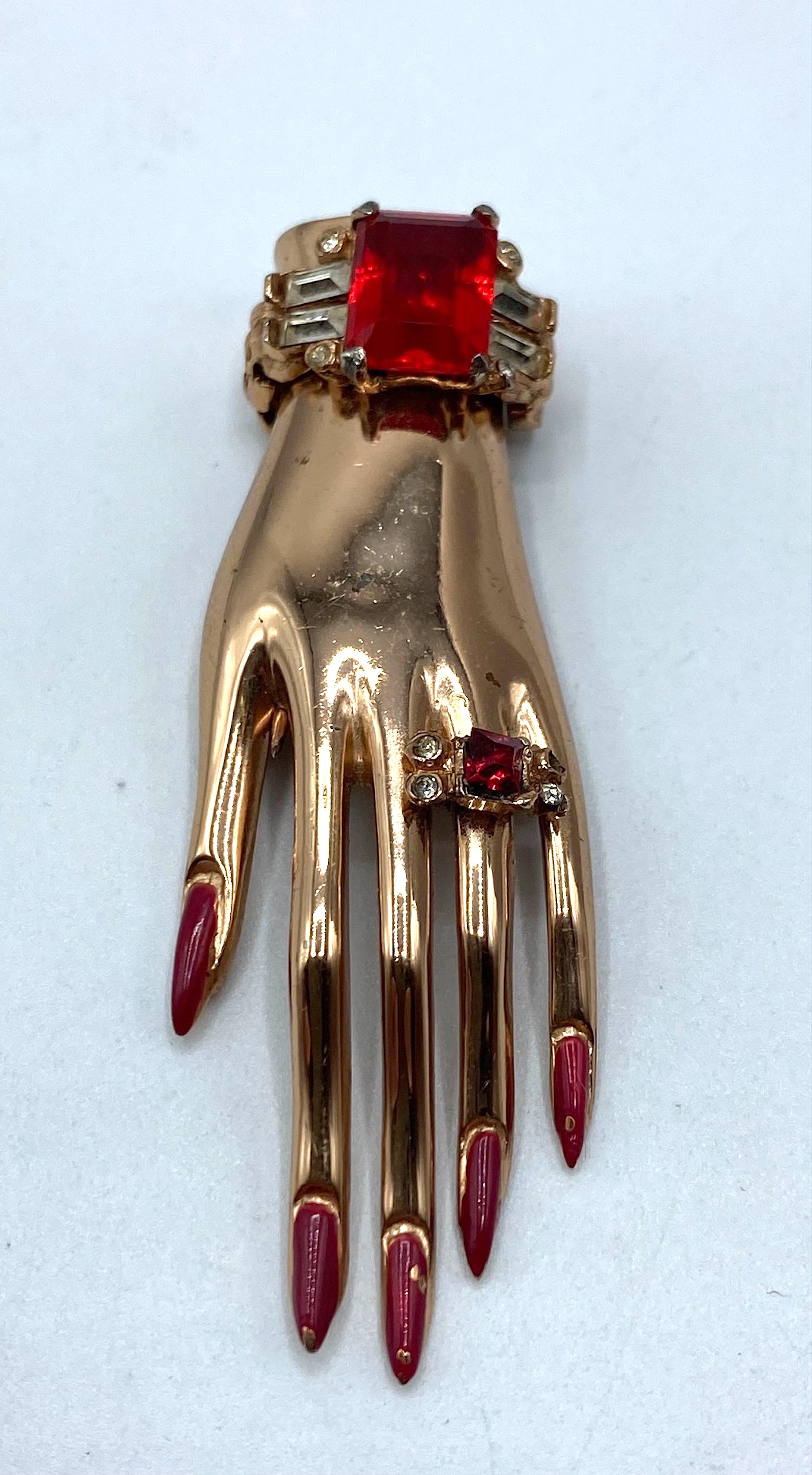 The Coro Craft large rose gold on sterling silver with red rhinestones hand fur clip / brooch is a notable piece designed and patented in 1944. This piece reflects a long-standing tradition of hand-themed jewelry, which has been popular for