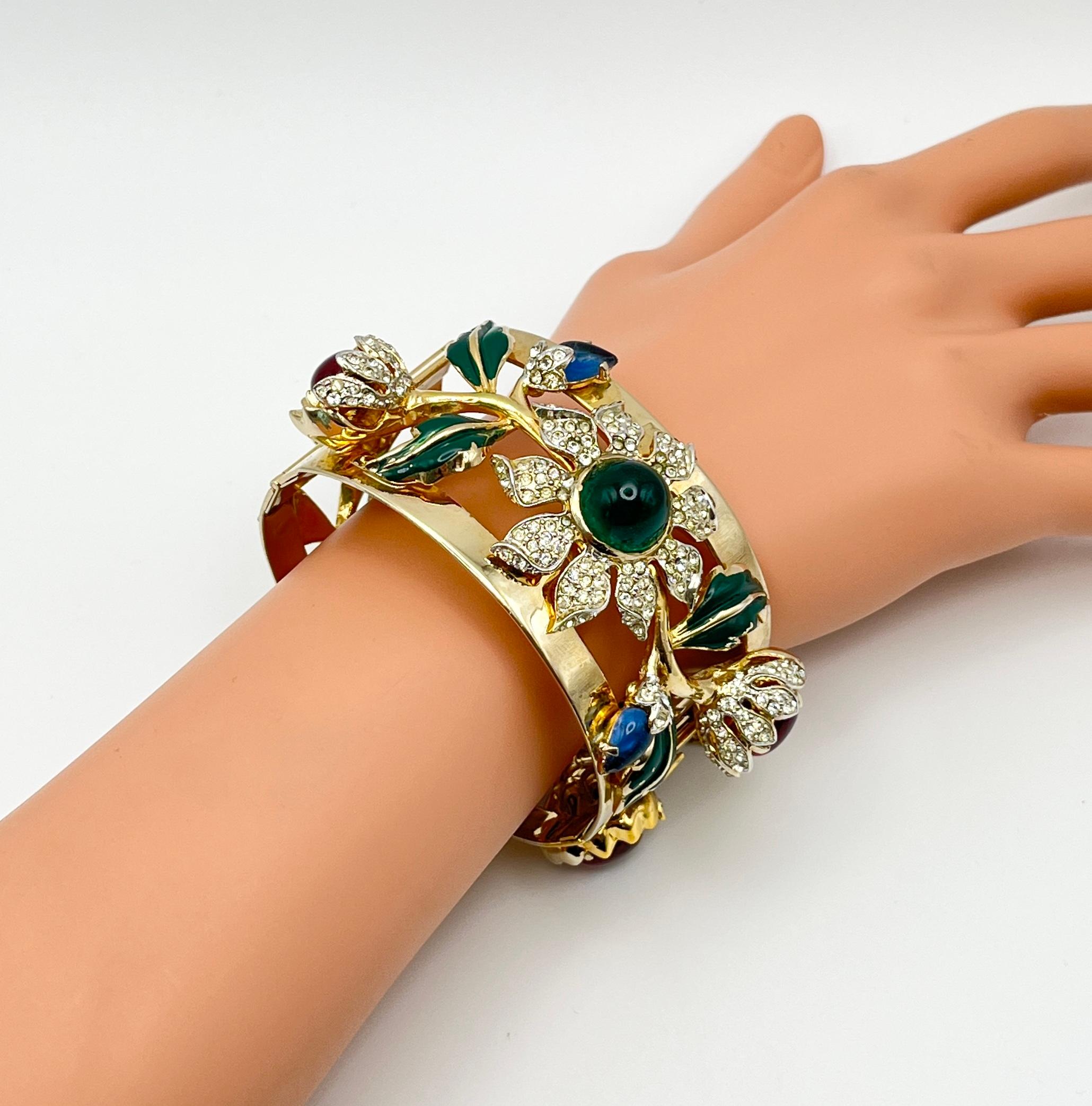 A bold and rare Corocraft bangle bracelet, dating to the 1940s, showcasing the brand’s signature opulent style and attention to detail. The wide hinged cuff is crafted in gilt metal with an openwork floral motif, adorned with pavé-set clear