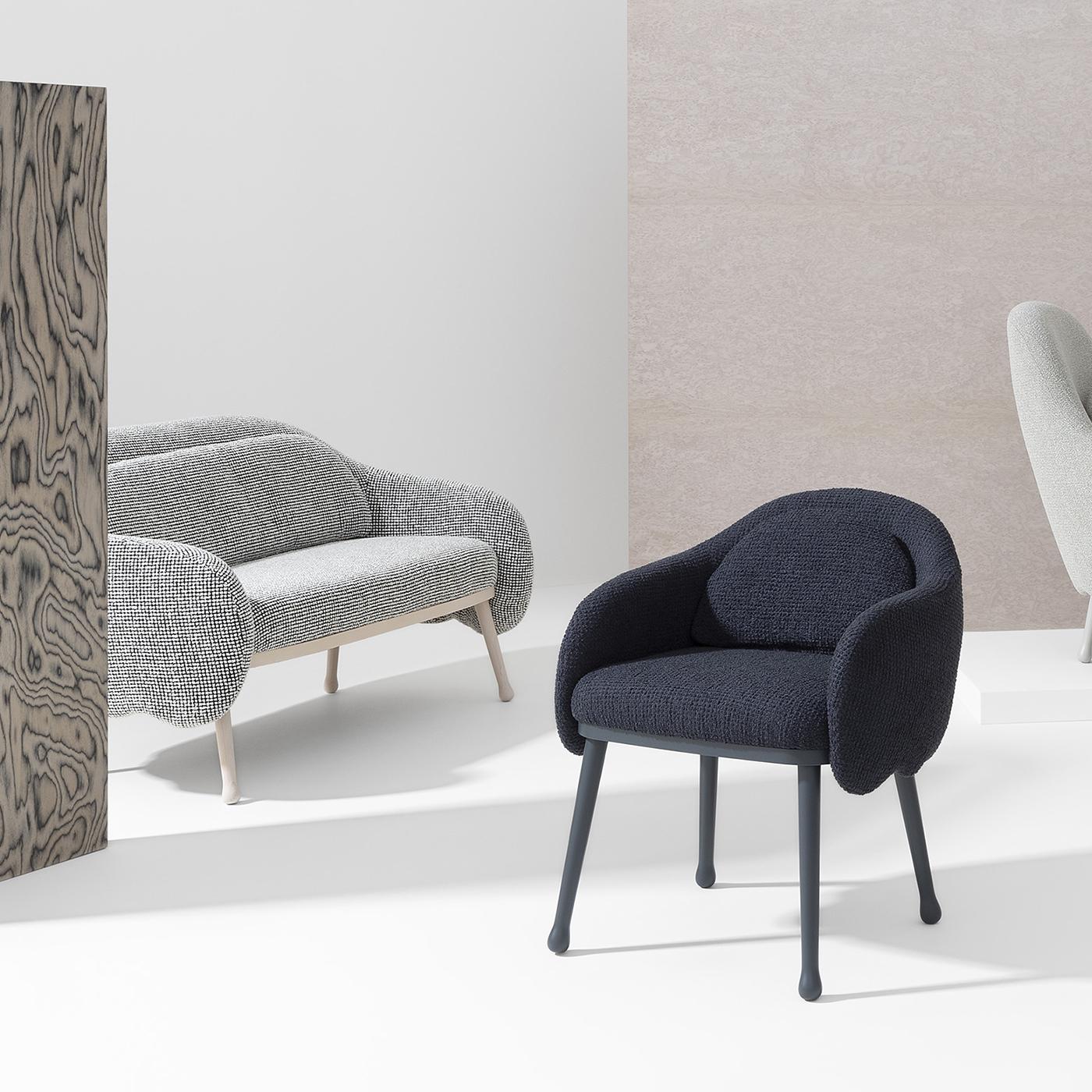 Exuding comfort and relaxation, this modern armchair is a superb design by Cristina Celestino. Resting on a solid beechwood structure with four black-lacquered legs with round feet and felt pads, the seat is softly padded and features a black fabric