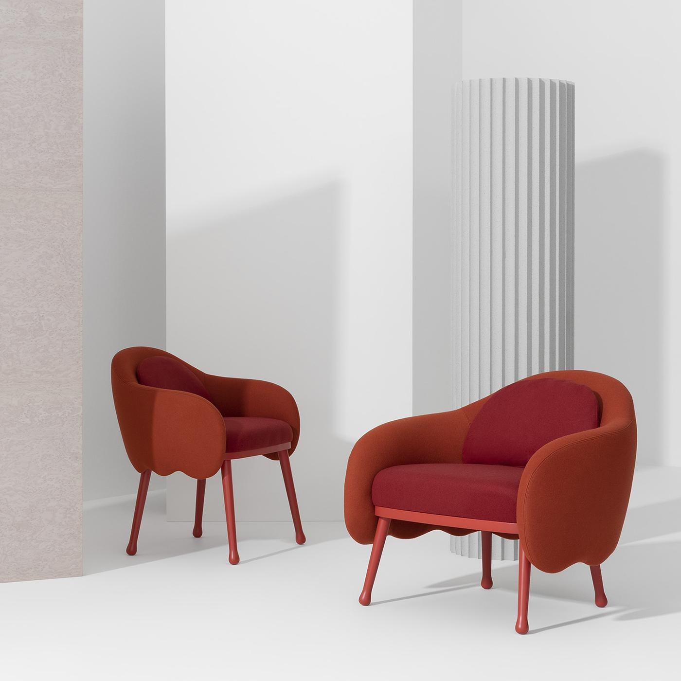 Characterized by an exquisite combination of warm hues, this armchair features two different upholsteries: a red fabric covering the seat and back cushions, and an orange one for the waved backrest and armrests. An exquisite modern design by