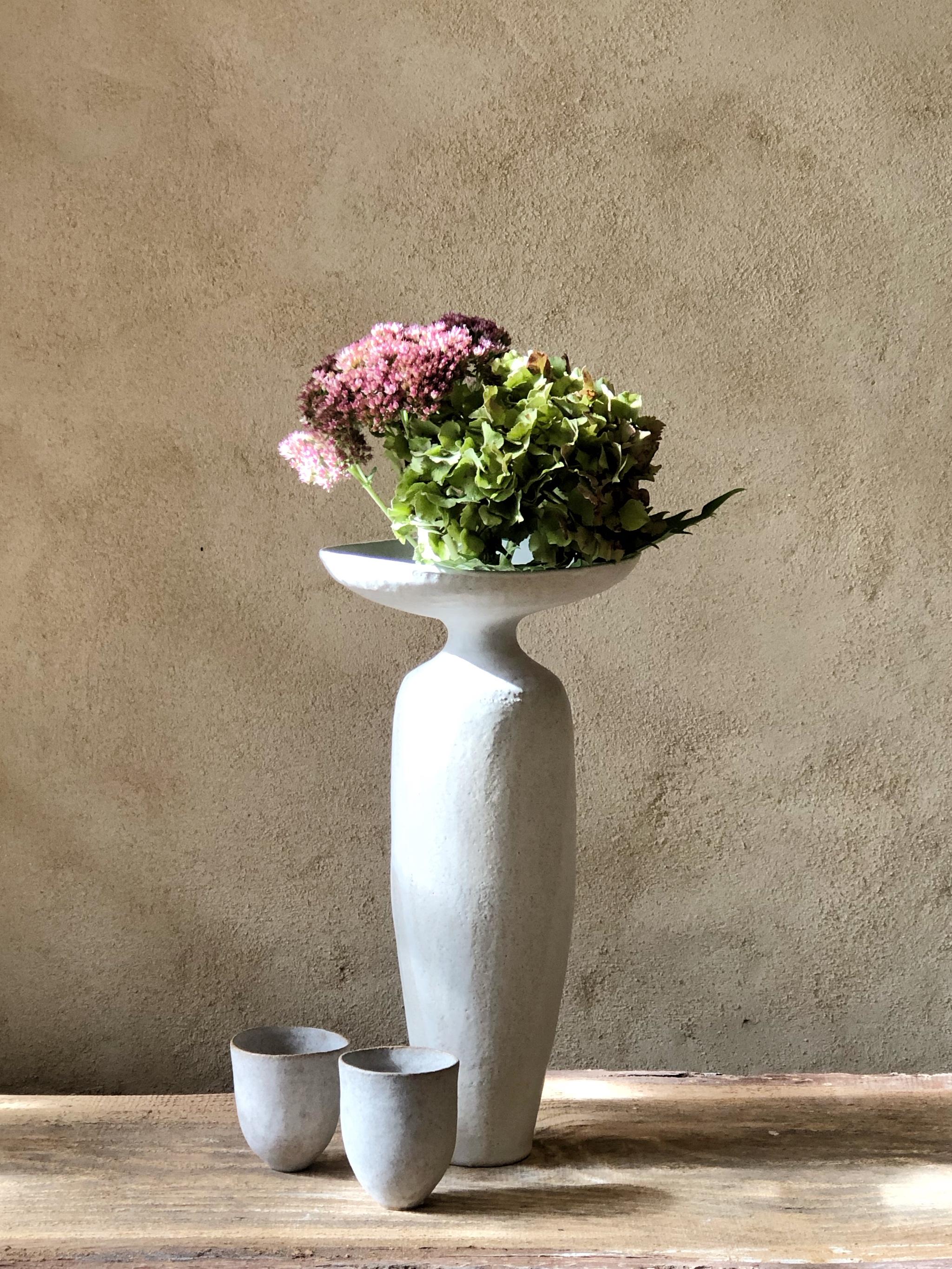 Corolla-Vase von Sophie Vaidie
Einzigartig.
Abmessungen: Ø 15 x H 35 cm. 
MATERIALIEN: Beigefarbenes Steinzeug mit weißer matter Glasur.

Am Anfang stand das Bedürfnis, mit den Händen, dem Tastsinn, den Sinnen zu arbeiten. Dann kam der Wunsch auf,