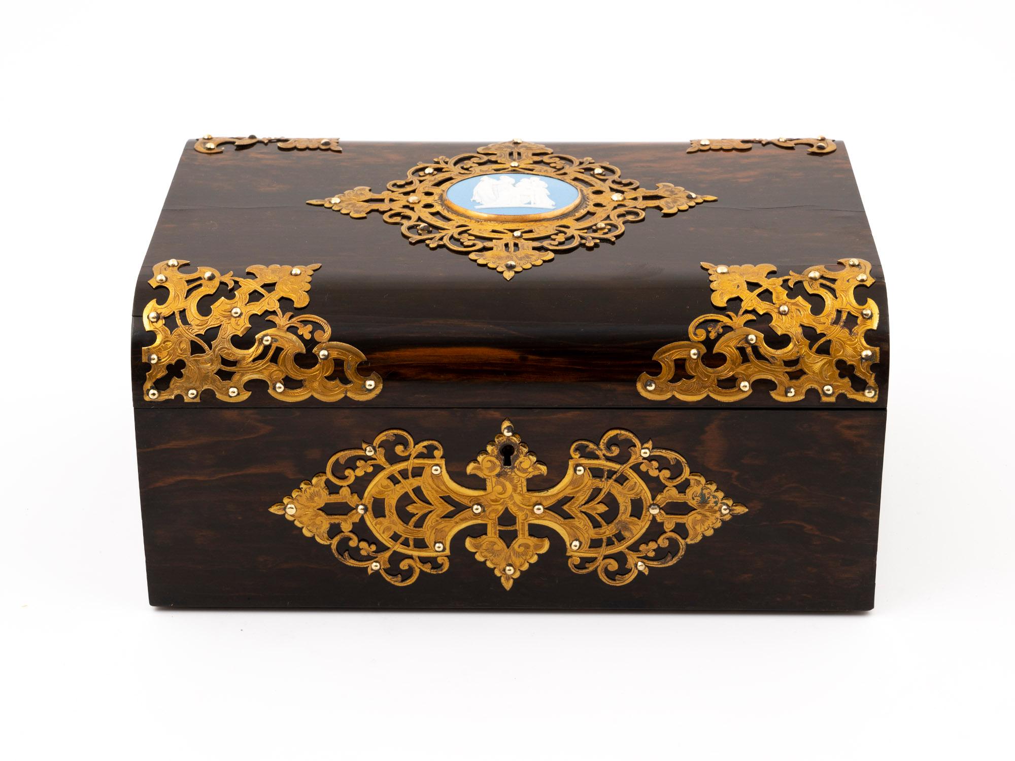 Behold the exquisite Coromandel dome-topped antique jewellery box, crafted by none other than Betjemann & Son, renowned for their unparalleled craftsmanship.

The box features stunning applied ornately engraved brass gilded mounts on the top and
