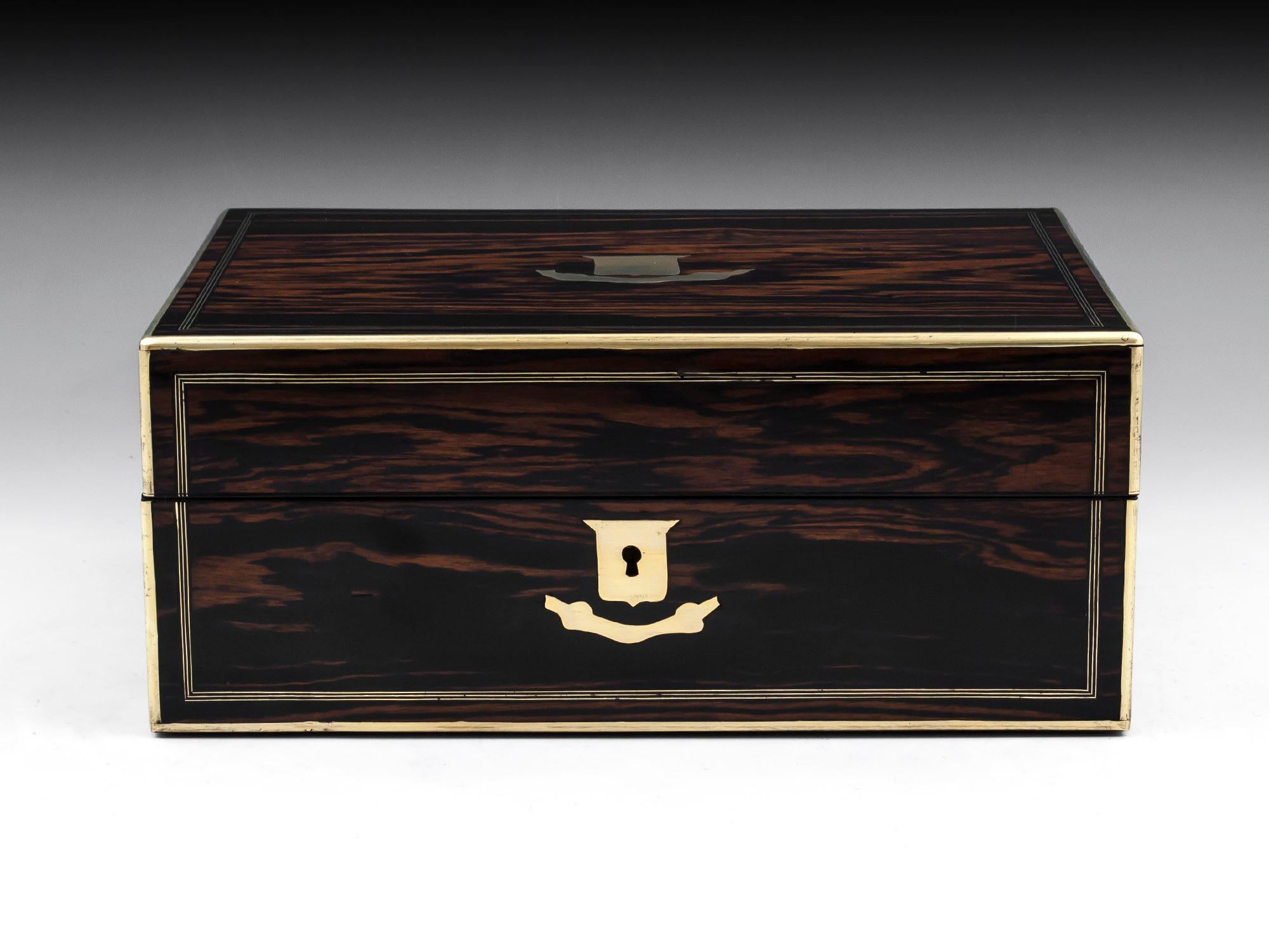 Jewelry box veneered in exotic figured Coromandel with brass quadrant edging and triple stringing on the front and top. With a brass shield escutcheon and matching vacant initial plate. 

The interior of this antique jewelry box is lined in red