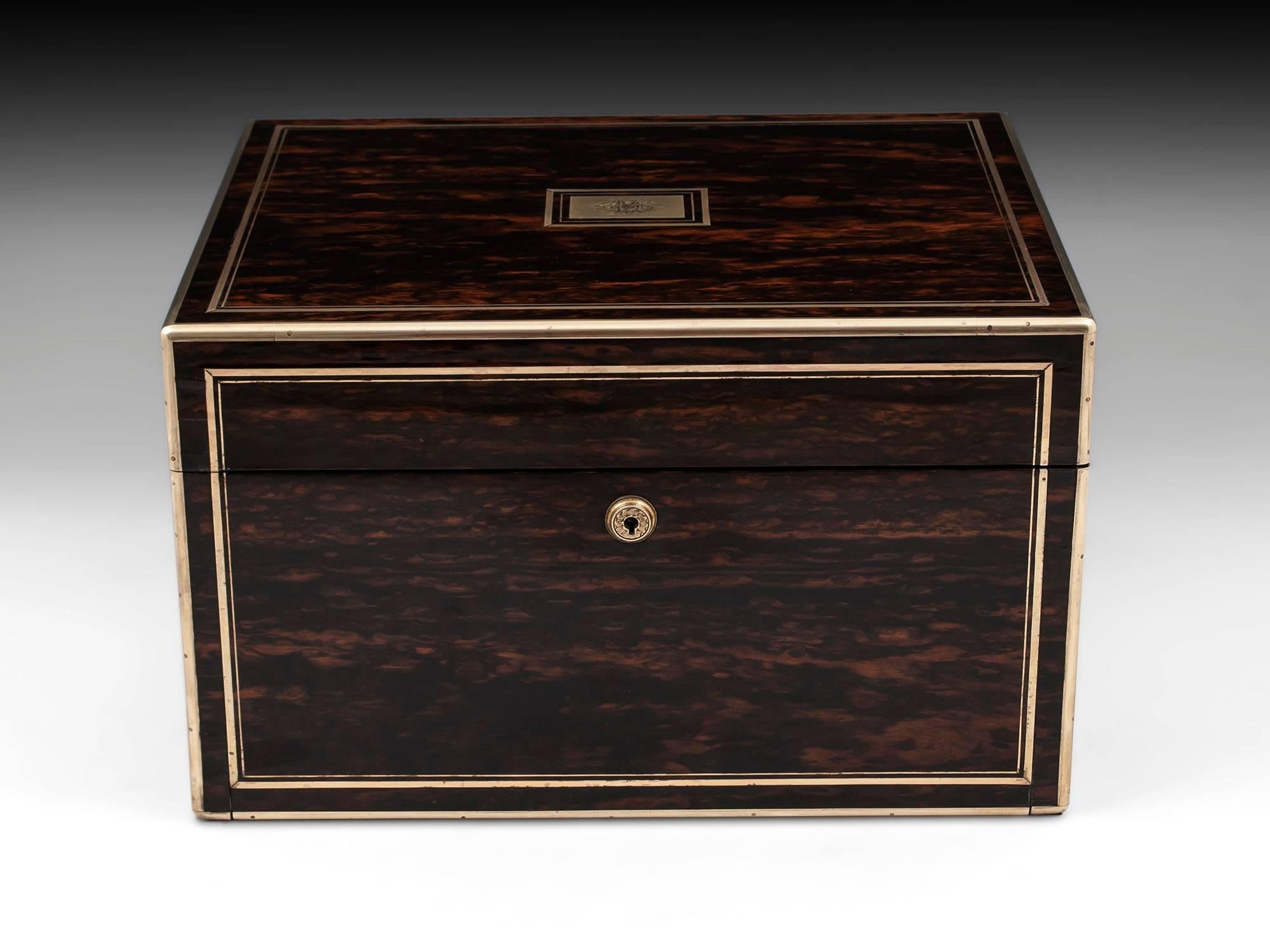 Sterling silver vanity box veneered in stunning Coromandel, bound and double strung in brass with robust campaign carry-handles and engraved escutcheon. The interior features twelve hobnail cut glass containers with elaborately engraved silver lids