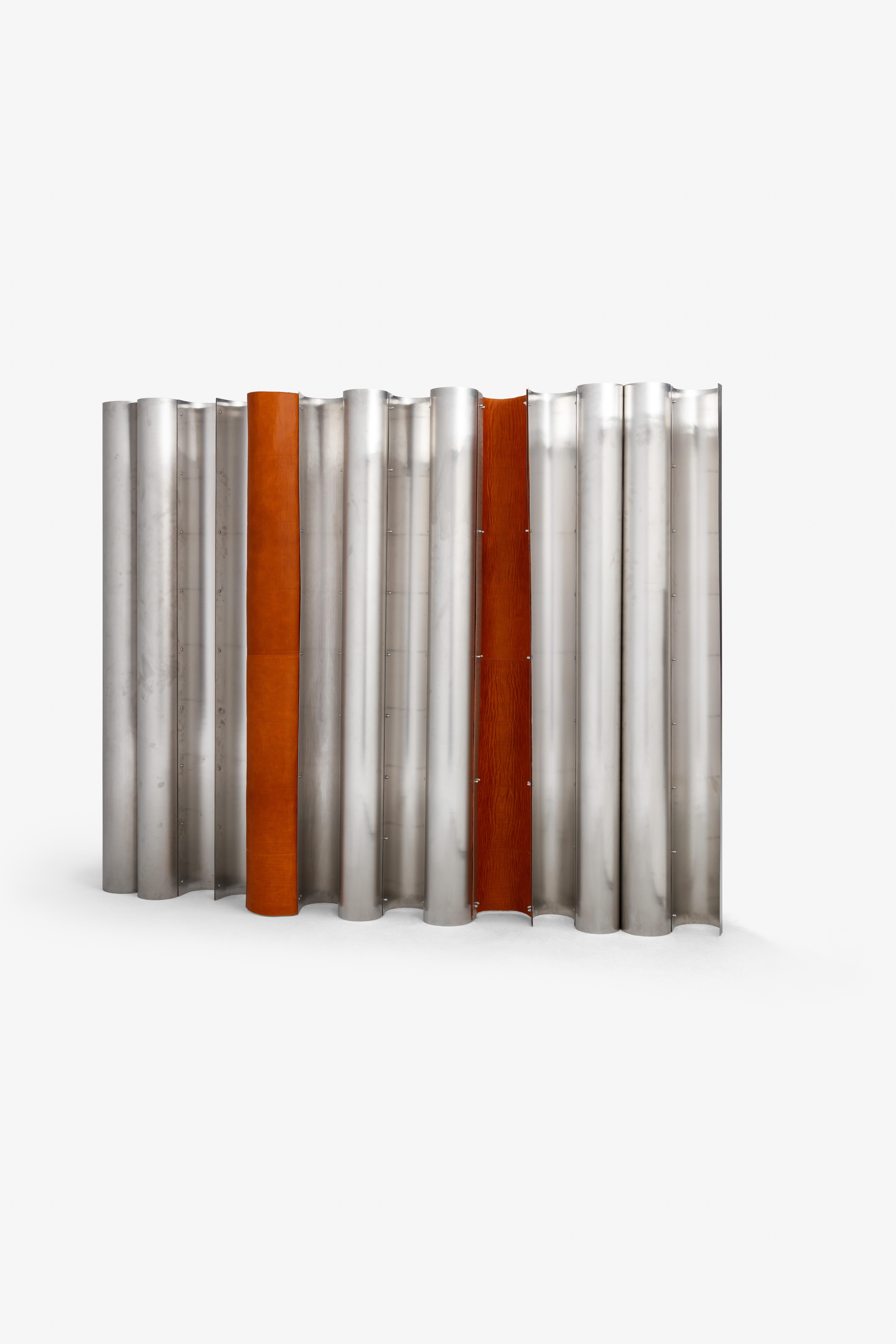 Composto da pannelli ondulati in acciaio inossidabile con inserti verticali in pelle, questo pezzo funziona sia come divisorio che come scultura. Il gioco di metallo e pelle aggiunge morbidezza e tattilità, riflettendo l'esplorazione di Simões del