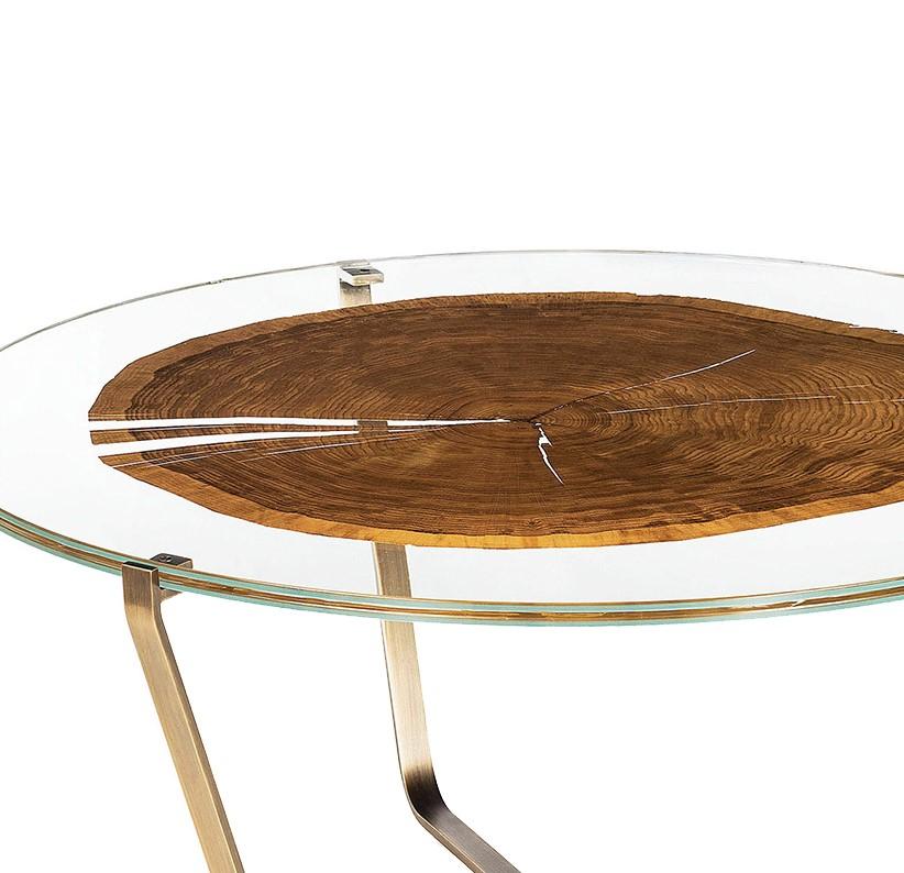 Part of the glass and wood collection, this modern and sophisticated coffee table rests on a structure that is comprised of three metal legs. The round top is made of two layers of glass that enclose a section of tree slice. The wood adds a warm,