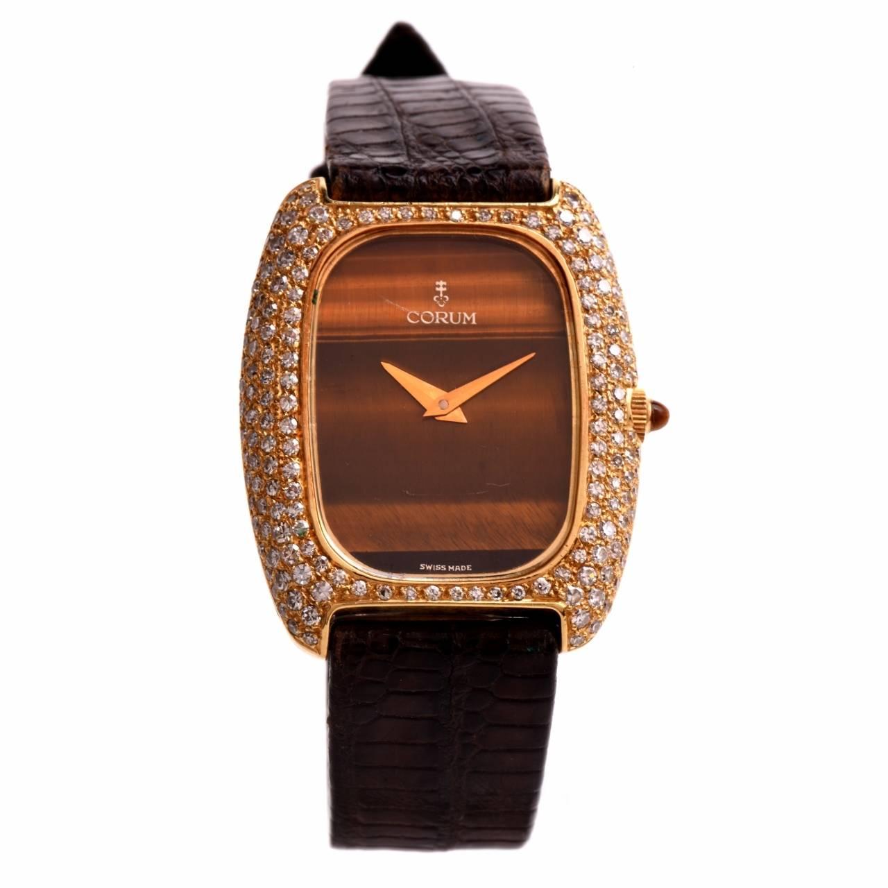 This 1960's Corum wristwatch with a diamond bezel and a tiger's eye dial is crafted in 18K yellow gold. The case measures 35 mm x 30 mm. The eye-catching stylized rectangular case is adorned with 3.00 cts of pave diamonds graded H-I color and VS