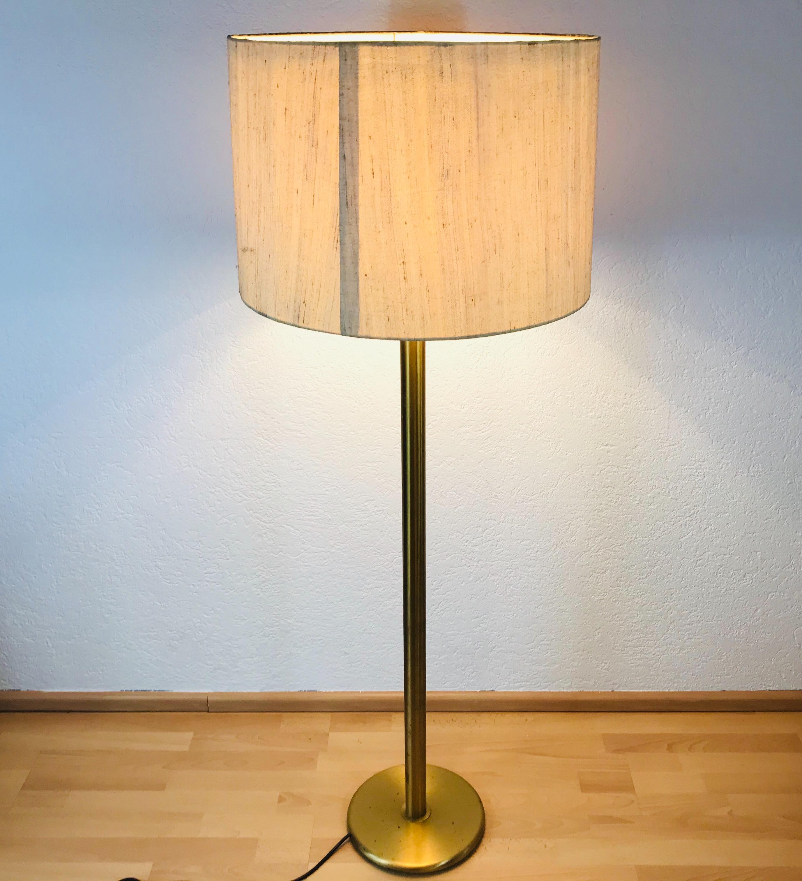 A midcentury floor lamp by Cosack made in Germany in the 1960s. It is fascinating with its midcentury design and cloth shade. The bottom of the light and the bar are made of full brass there are three E27 sockets on the bar and one E27 socket on the