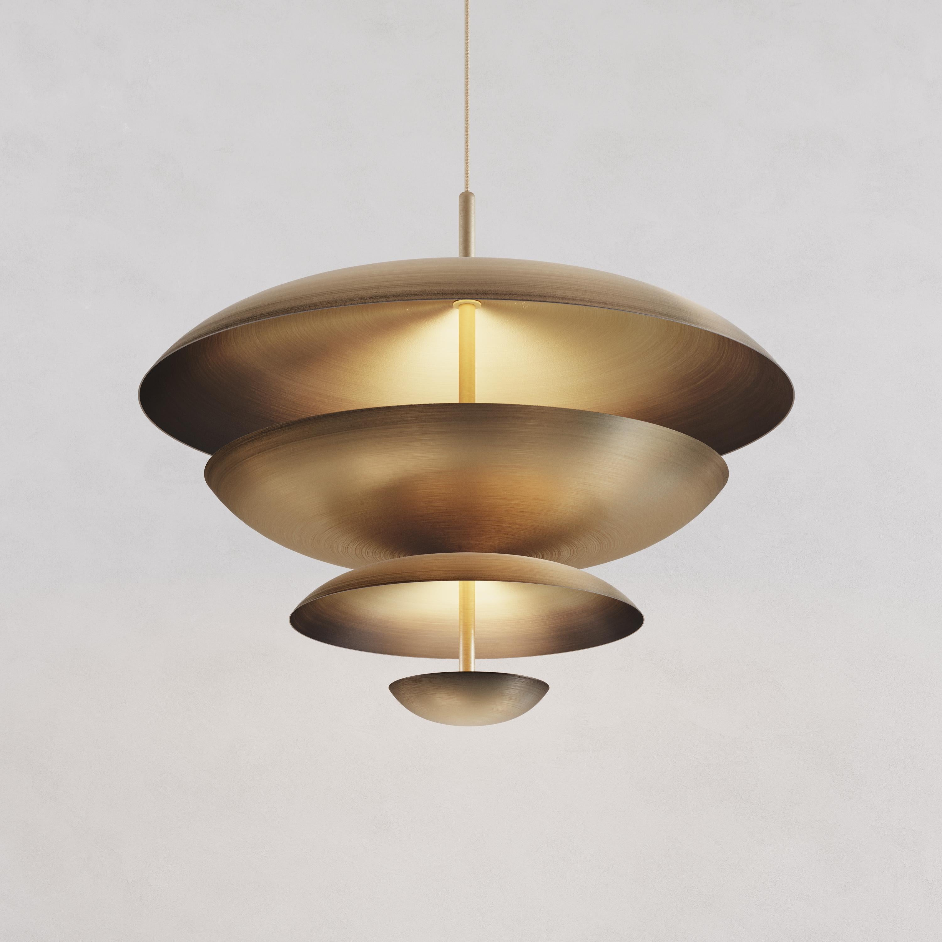 Finely hand-spun brass plates make up this pendant light, finished with a gentle gradient patina. Both sides of the brass shades are bronzed and gently brushed to reveal bright brass. The light is projected into the shade and reflects out,
