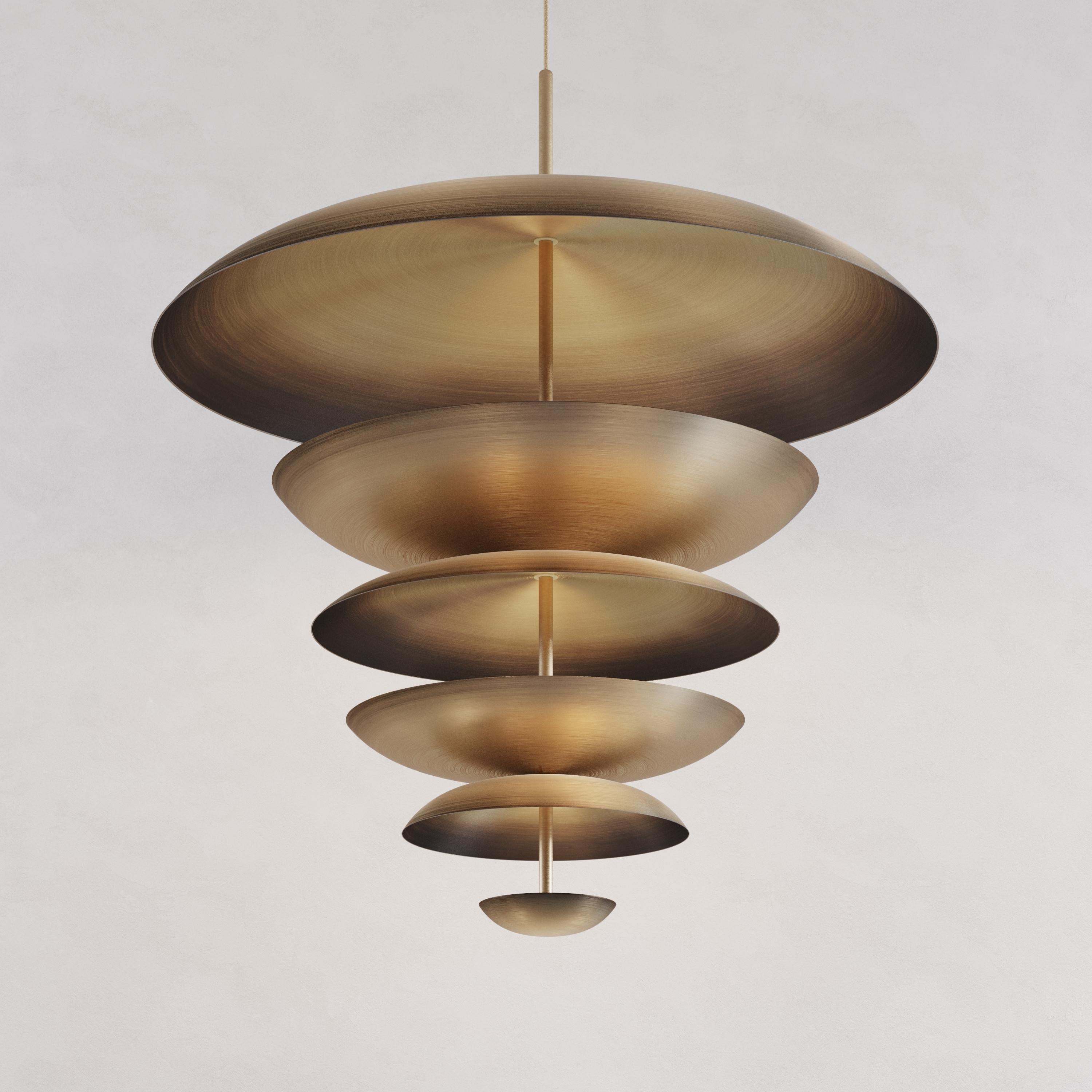Finely hand-spun brass plates make up this pendant light. One side of the plate is finished in a bronze gradient patina while the other side in a gently brushed brass gradient. The light is projected into the shades and reflects out, illuminating