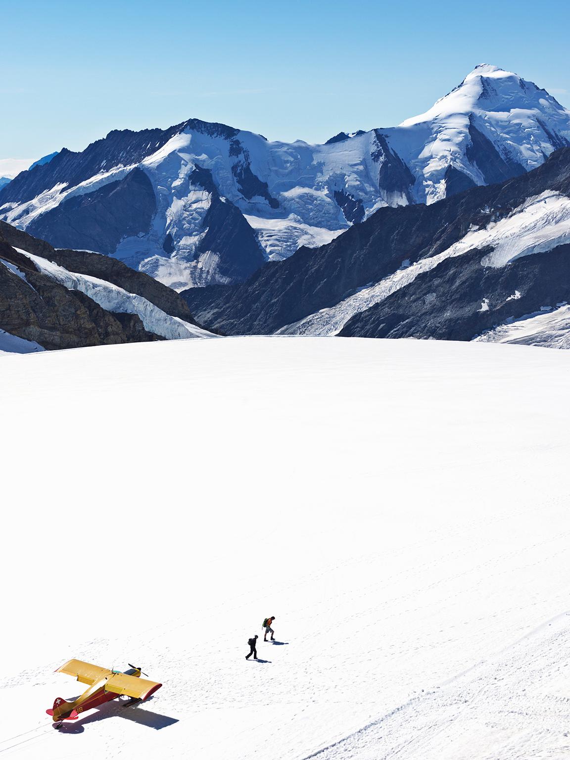 
Switzerland Jungfraujoch-Top of Europe. Airplane on glacier with mountains in background and two people walking away. The Great Aletsch Glacier. Creation Year 2008, Archival Pigment Print 18