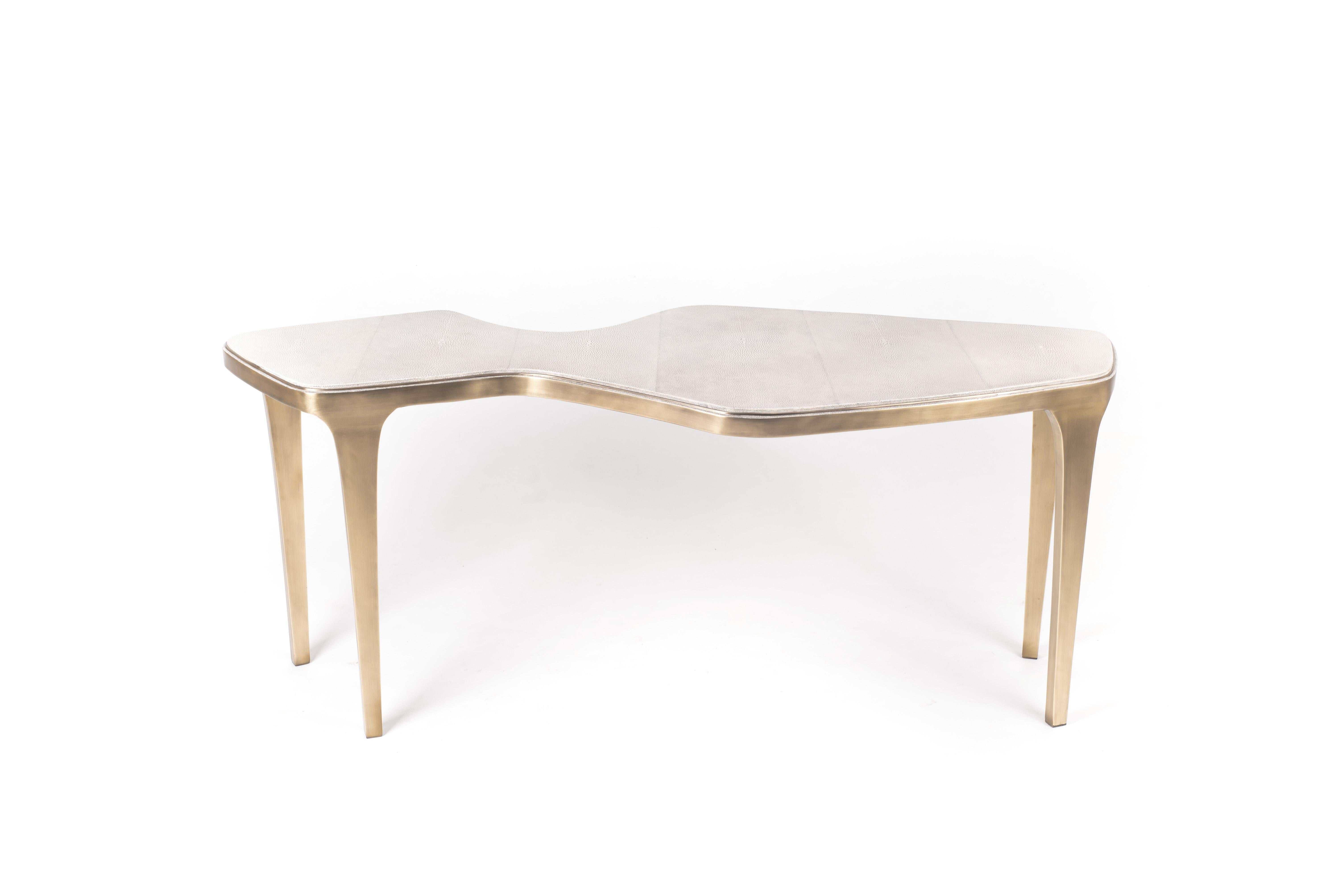 Cette annonce concerne uniquement la grande table gigogne. La grande table basse gigogne cosmos est à la fois minimaliste et spectaculaire. Le plateau est incrusté de galuchat crème, teinté à la main par les artisans, et complété par du laiton