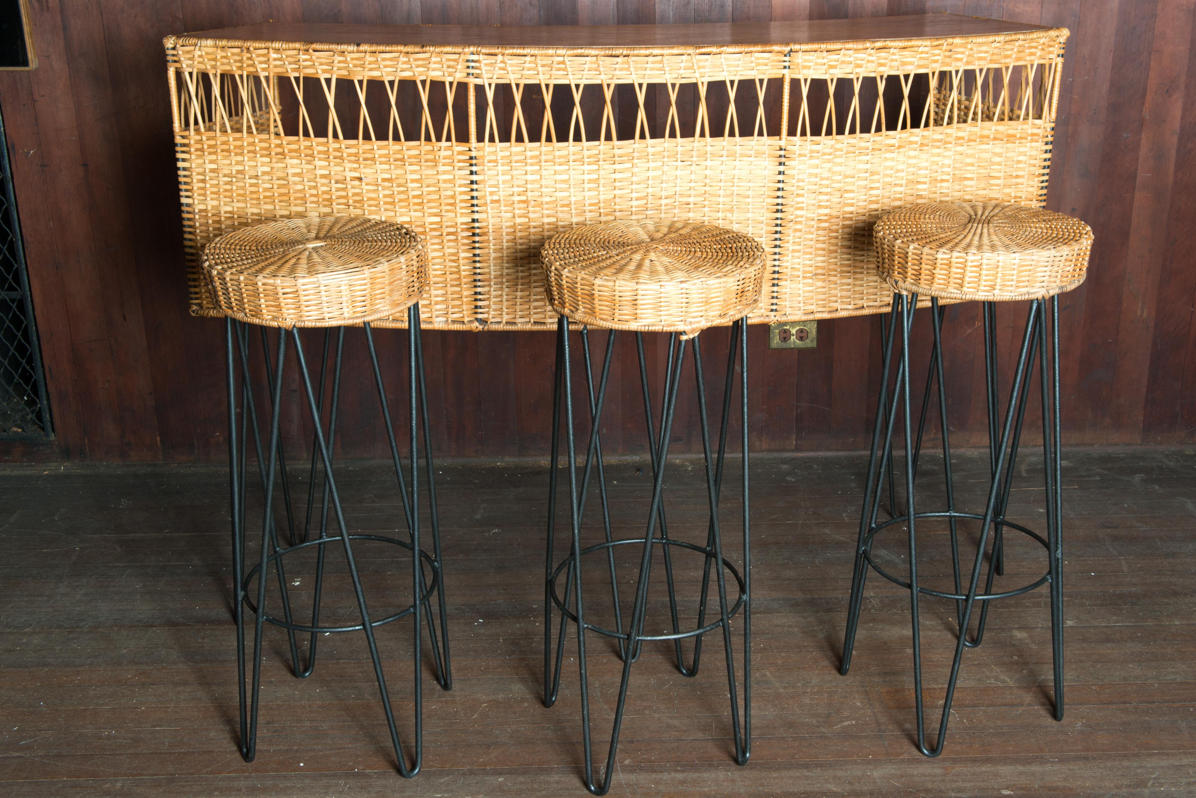 A spectacular South of France rattan bar and three stools, all with glamorous black wrought iron hair pin legs. The designer of this stunning curved bar and stools is Rauol Rhieys. The curved bar top is wood. The woven work is beautiful and in