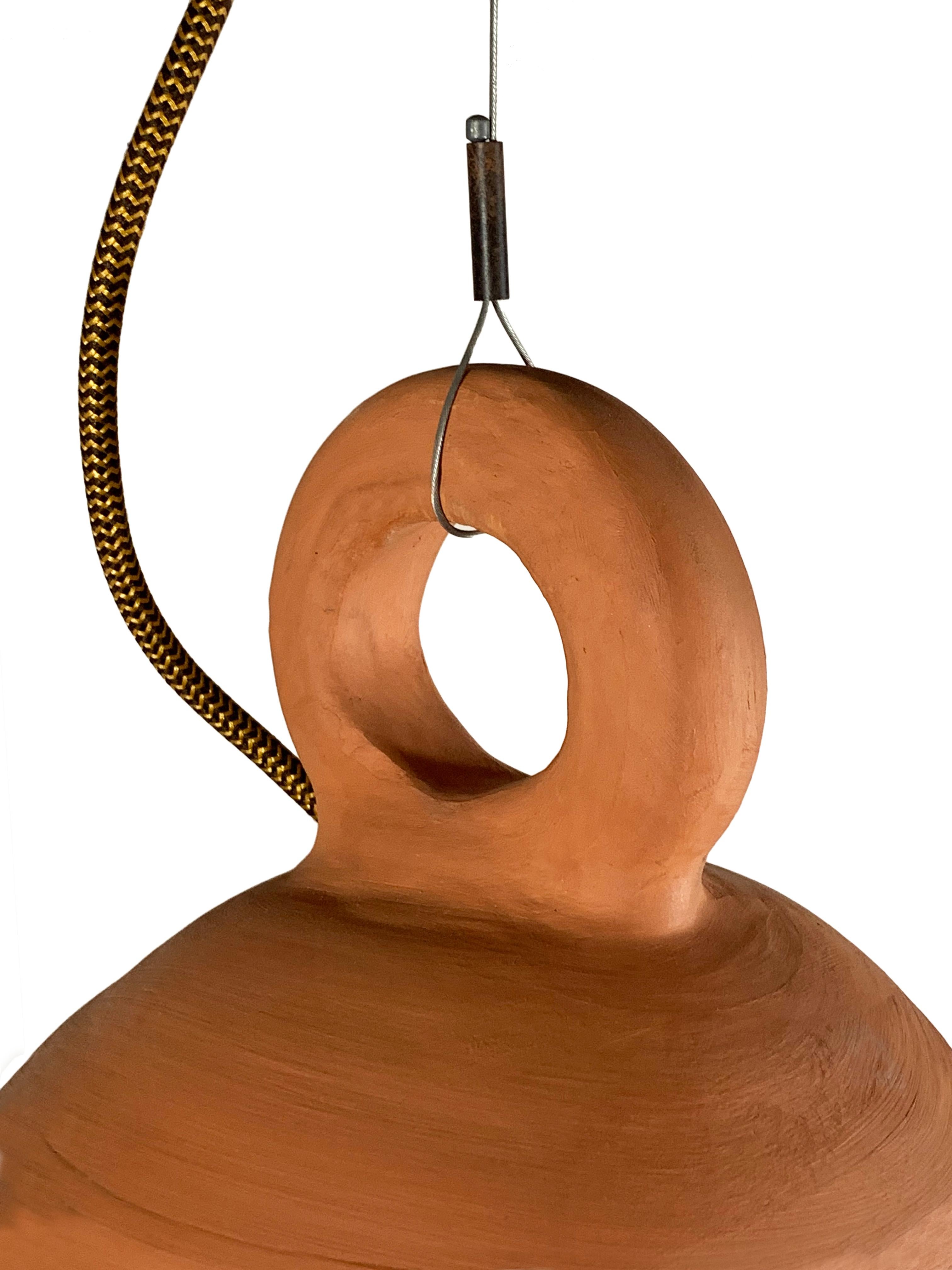 Terracotta pendant, handmade in Ibiza. Suspended by slim, adjustable height stainless steel cable and wired with cloth-covered herringbone electrical cable. Metal ceiling rose with terracotta paint finish. E27 bulb holder.
Light bulb casts a warm