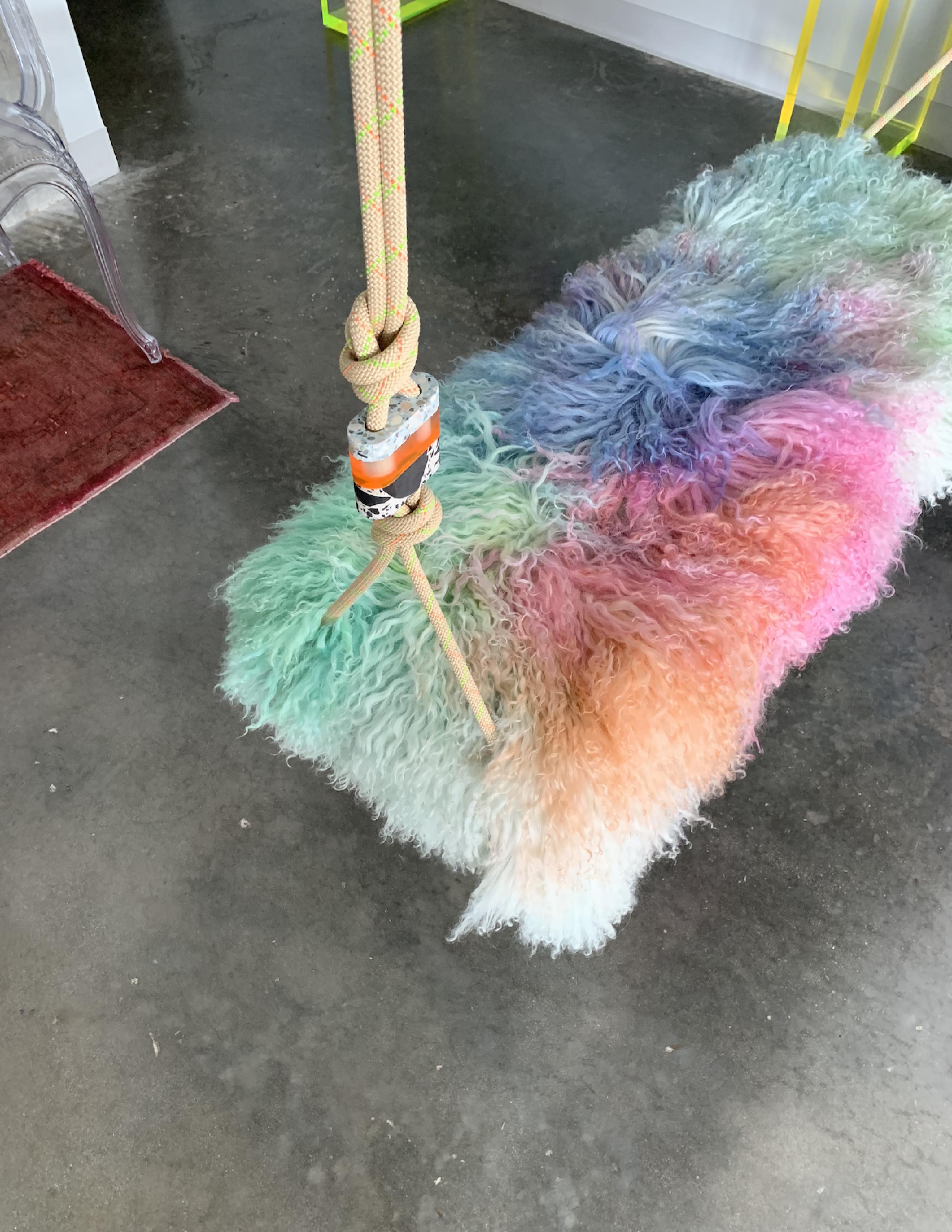 The cotton candy swinging bench is a playful indoor swing for two featuring a Tibetan Lamb cushion, colorful accessory cord, a Lucite base and Lucite accessories. Featured here is a fun, multi-color Tibetan Lamb, however, there are a variety of