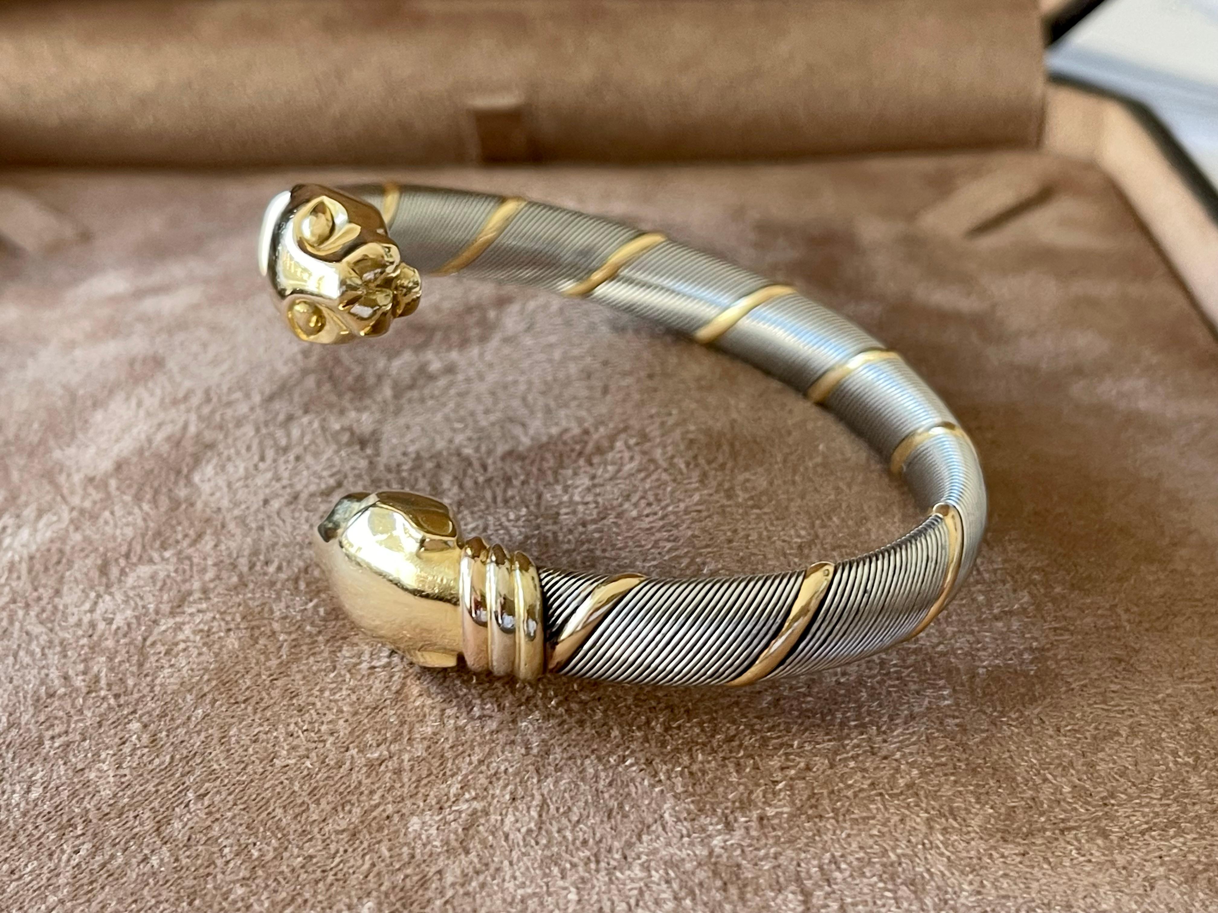 A beautiful vintage 1980’s Panthère de Cartier bangle set in stainless steel and 18 K yellow white and rose Gold.
This incredibly stylish bangle is composed of two solid yellow gold panther heads. These heads are connected to a coiled stainless