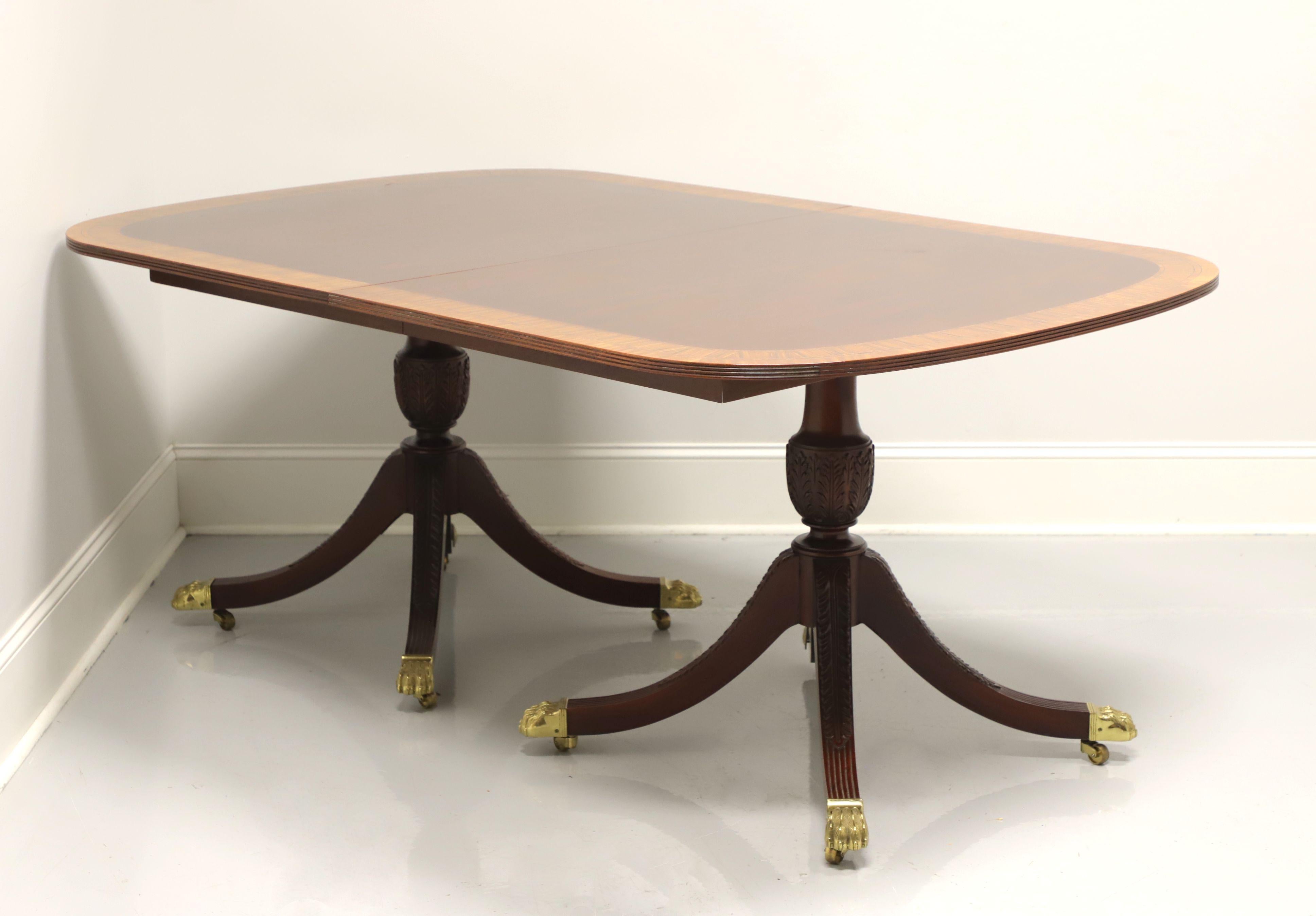 A Traditional style double pedestal dining table by Councill Craftsmen. Mahogany with a cross-banded rounded corners top, wood expansion sliders, carved double pedestal with four carved legs, brass toe-caps and casters. Includes two extension