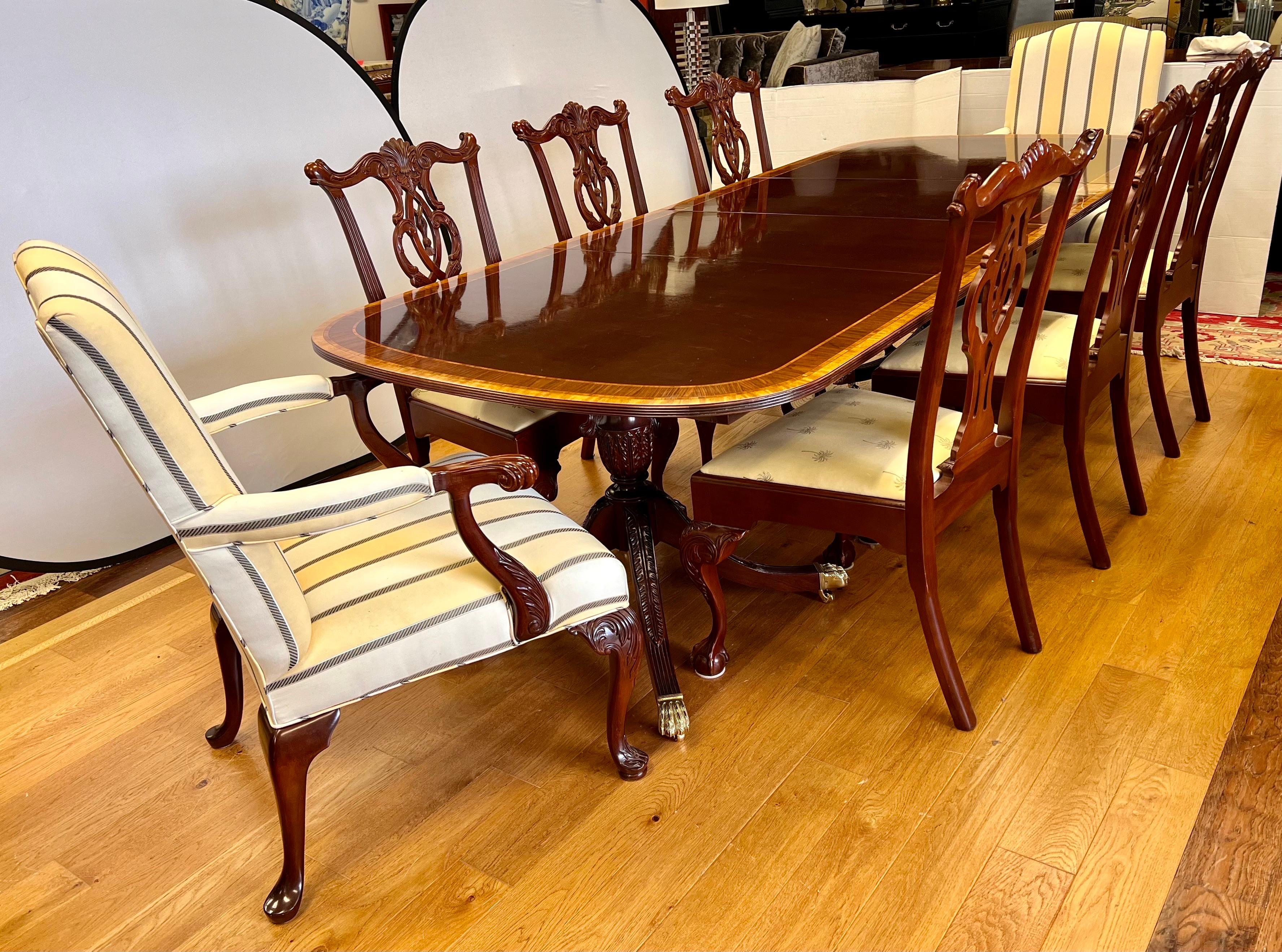Elegant Councill Craftsman banded mahogany double pedestal dining room table on brass castors for ease of movement. There are eight chairs total, 6 carved mahogany side chairs with ball and claw feet and 2 large upholstered armchairs as shown. There