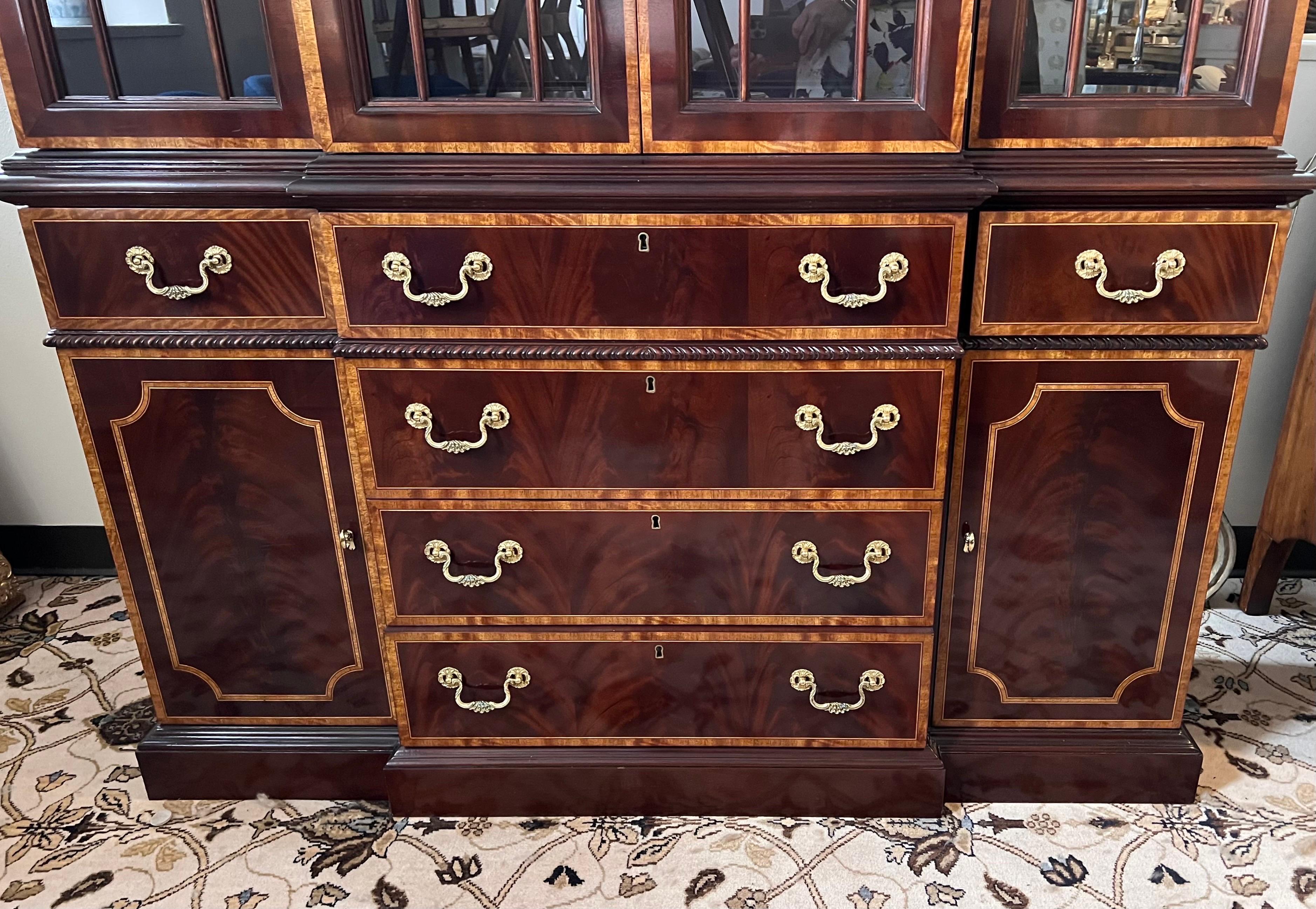 An exquisite flame mahogany china breakfront by Councill Craftsmen.  Features inlaid flame mahogany with ornate brass hardware, pediment with finial and dentil moulding to top of 2pc cabinet.  Upper cabinet is lighted and features nine glass shelves