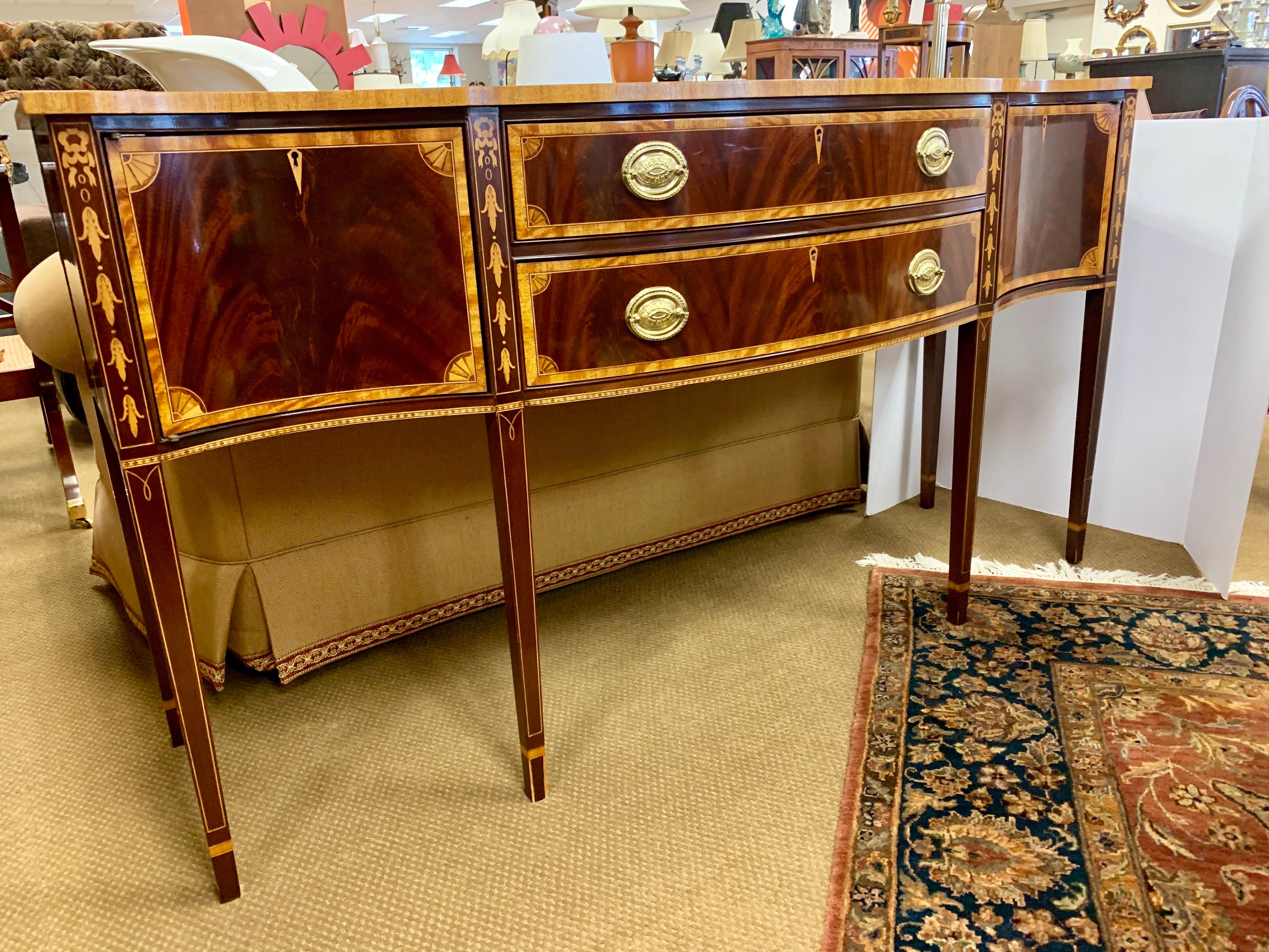 Elegant mahogany Councill Craftsman sideboard has multiple drawers and compartments and features gorgeous line and bell flower inlay. Has lockable drawers/compartments with two keys as well as felt-lined drawer for silverware.