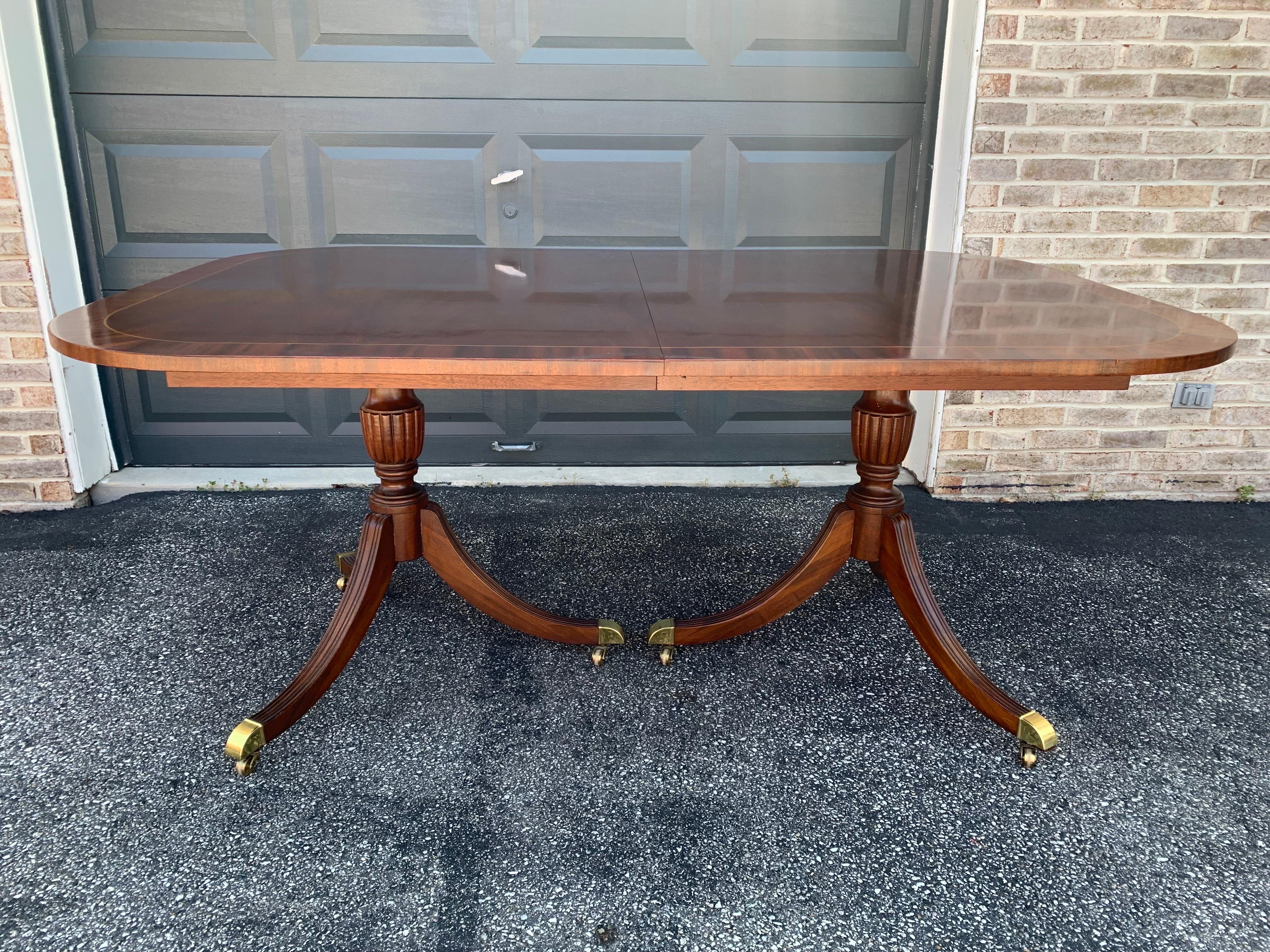 A gorgeous Georgian style double pedestal extension dining table manufactured by Councill Craftsman.

Beautiful mahogany with satinwood string inlay, carved solid mahogany pedestals, and brass-capped feet with original casters.

Measures: 68