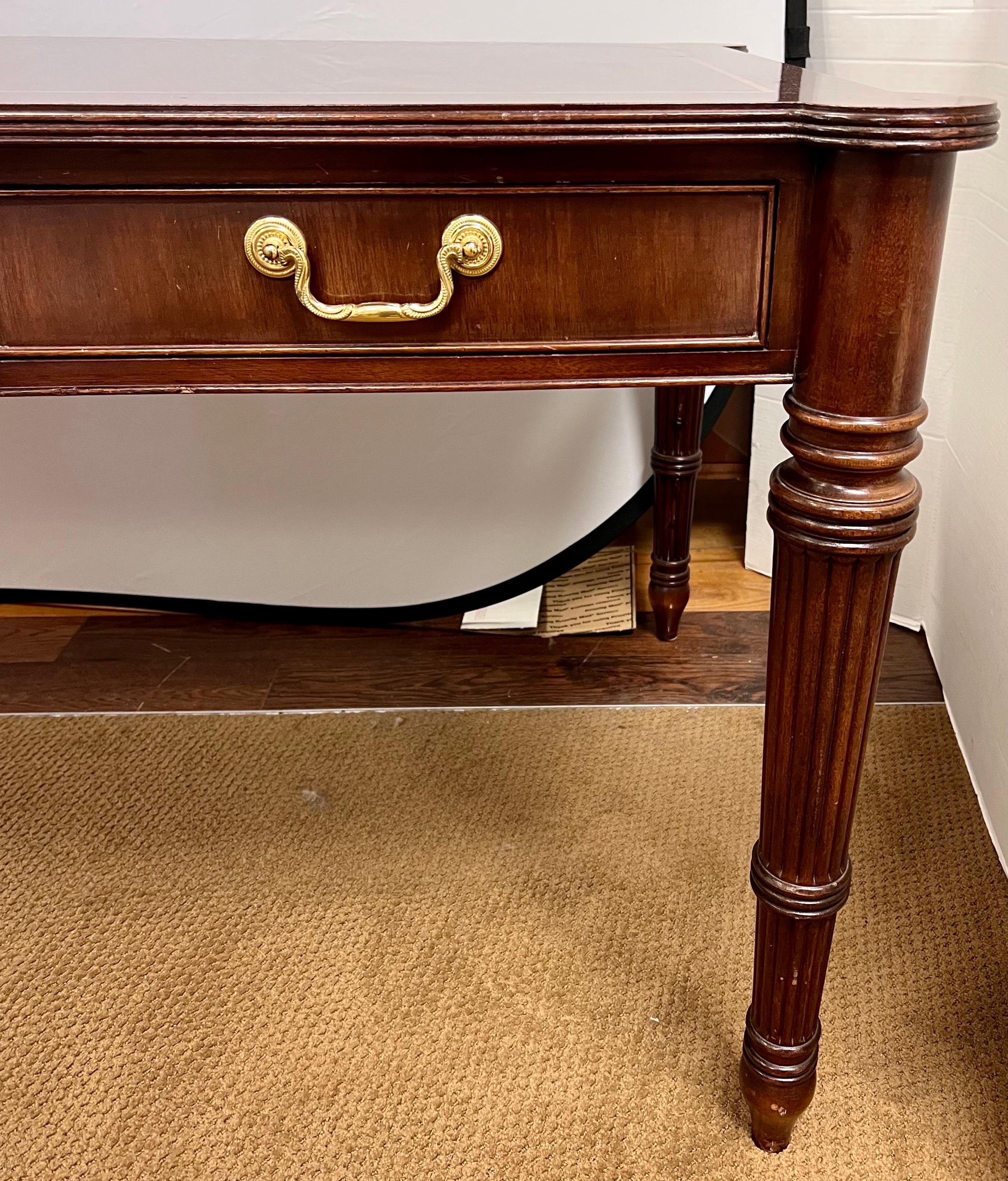 Classic handcrafted mahogany library or executive writing desk with three drawers and beautiful flame mahogany top on fluted legs.  All original brass pulls.  Removable custom protective glass top included.