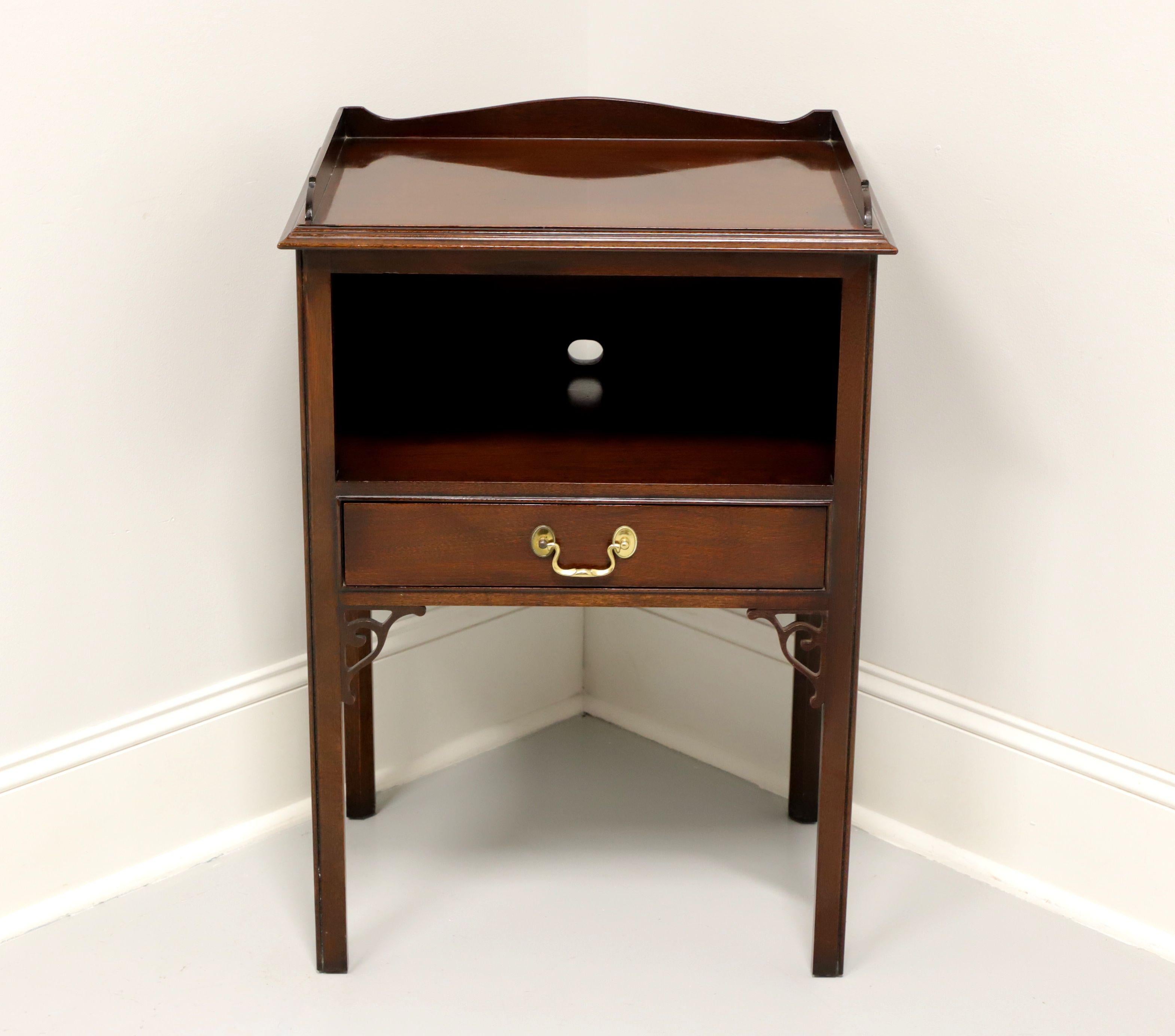 A Chippendale style nightstand by Councill Craftsmen. Solid mahogany, brass hardware, gallery to top, fretwork joins and straight legs. Features one dovetail drawer below an open storage area with a pre-drilled hole in back for electric cords. Made