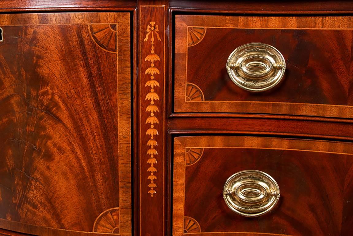 With a shaped top and two burled side cabinet doors with quarter fan corner inlays and escutcheons (with one key). Bell flower inlays separate the sides from the center two burled and banded drawers with leather linings, and with checked string