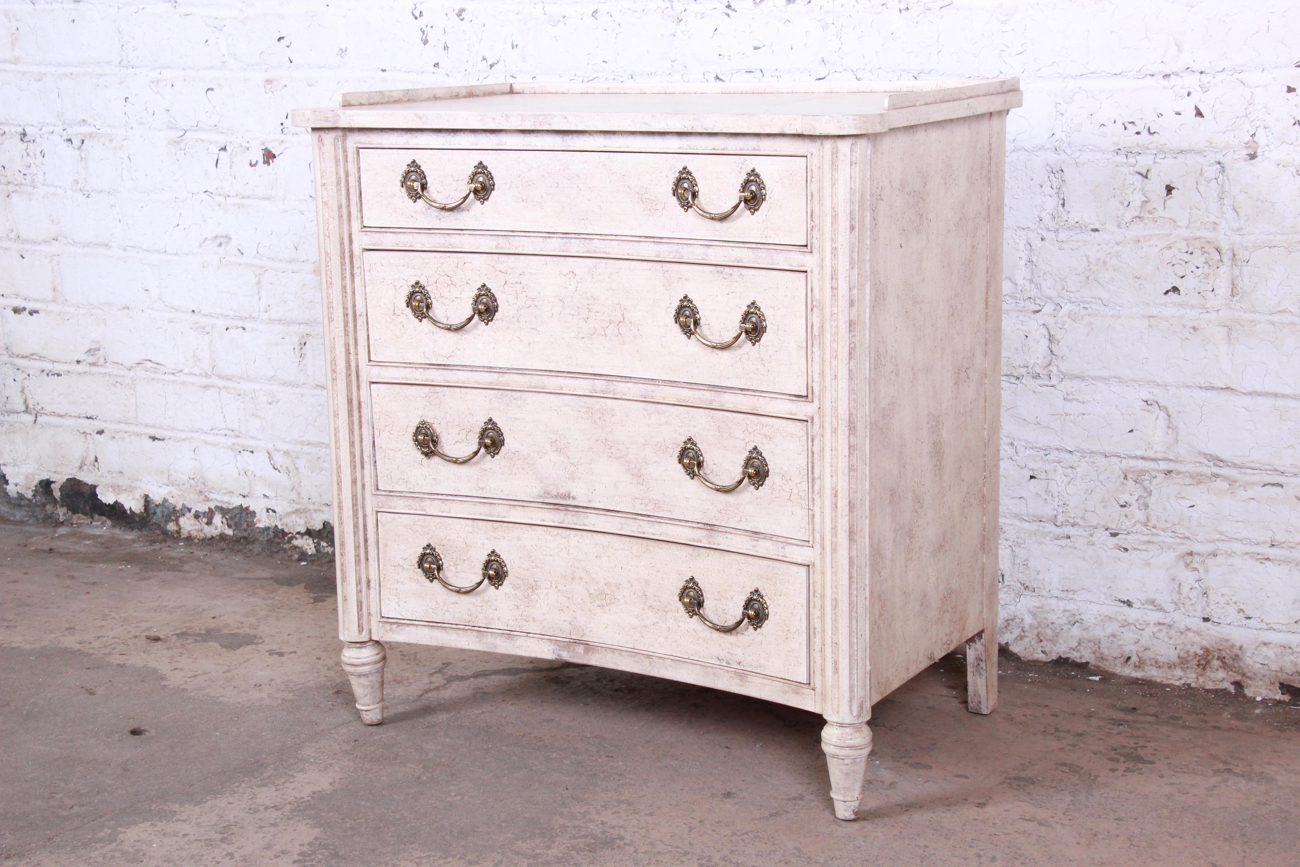 A gorgeous neoclassical style chest of drawers by Councill Furniture. The dresser features a beautiful original antiqued white finish. It offers ample storage, with four dovetailed drawers. Brass hardware is original, and the original Councill label