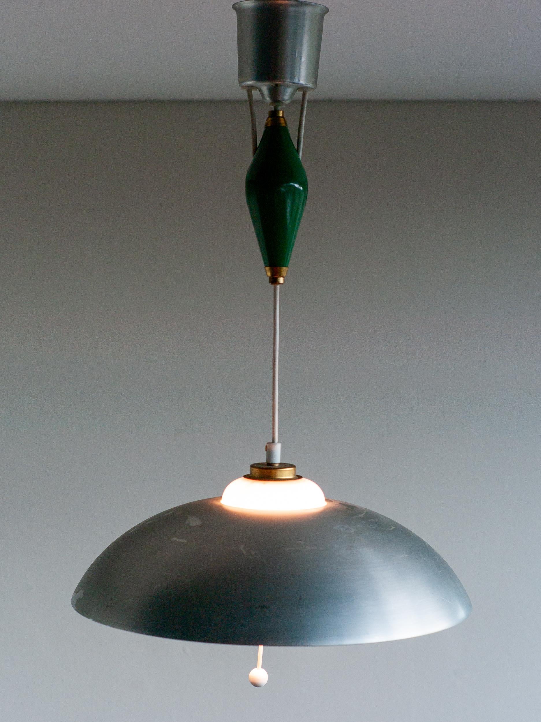 Magnifique pendentif ajustable de Nordiska Kompaniet fabriqué en 1950.
L'abat-jour et le cache plafond sont en aluminium poli. 
Le contrepoids est en porcelaine verte.
L'abat-jour intérieur est en verre blanc. La hauteur est variable. 
Marqué NK