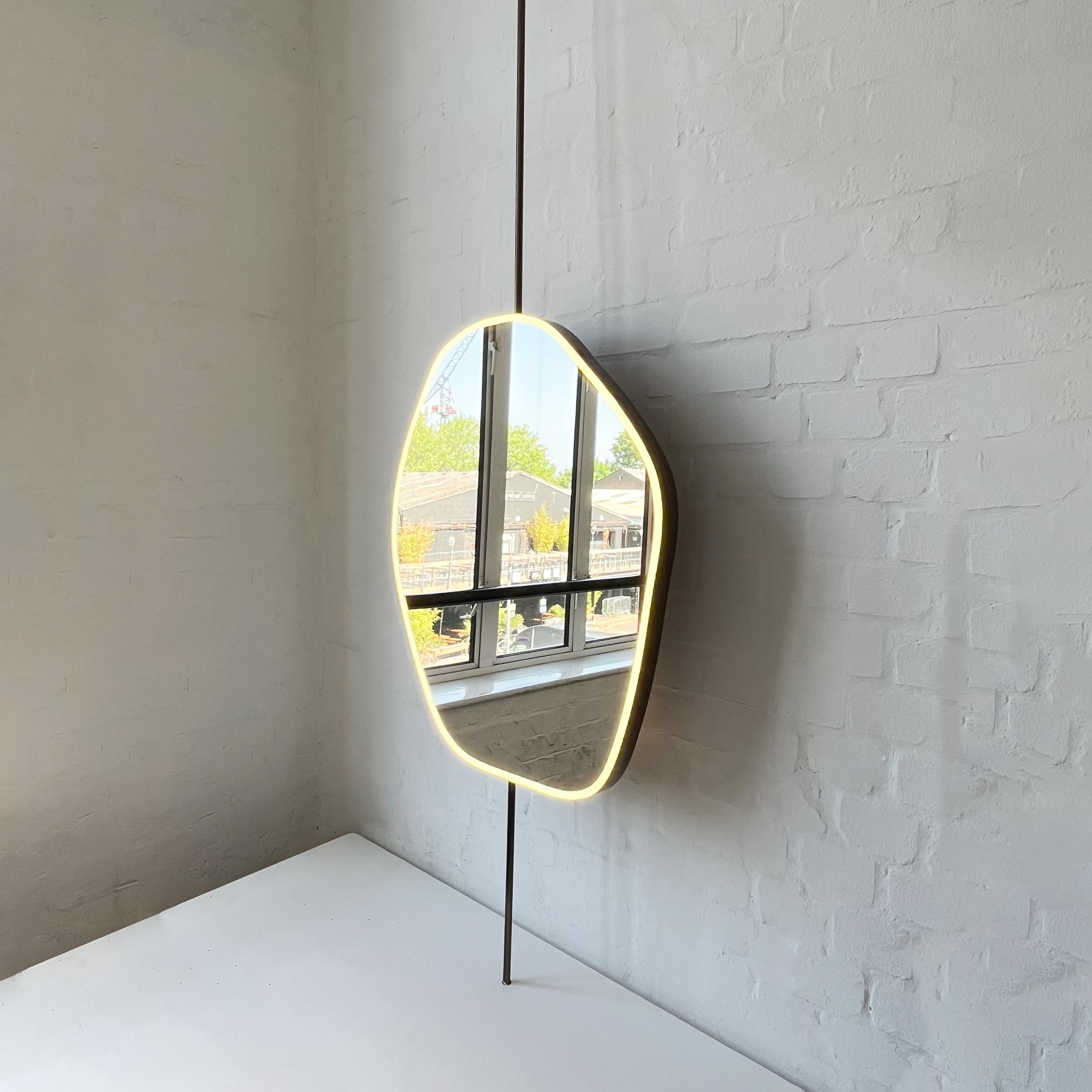 Contemporary countertop to ceiling attached freeform rotating mirror with a minimalist handcrafted bronze patina brass frame and front illumination. Designed and made in London, UK. This mirror is fully customisable.

Dimensions:

H 77cm x W 61.5cm
