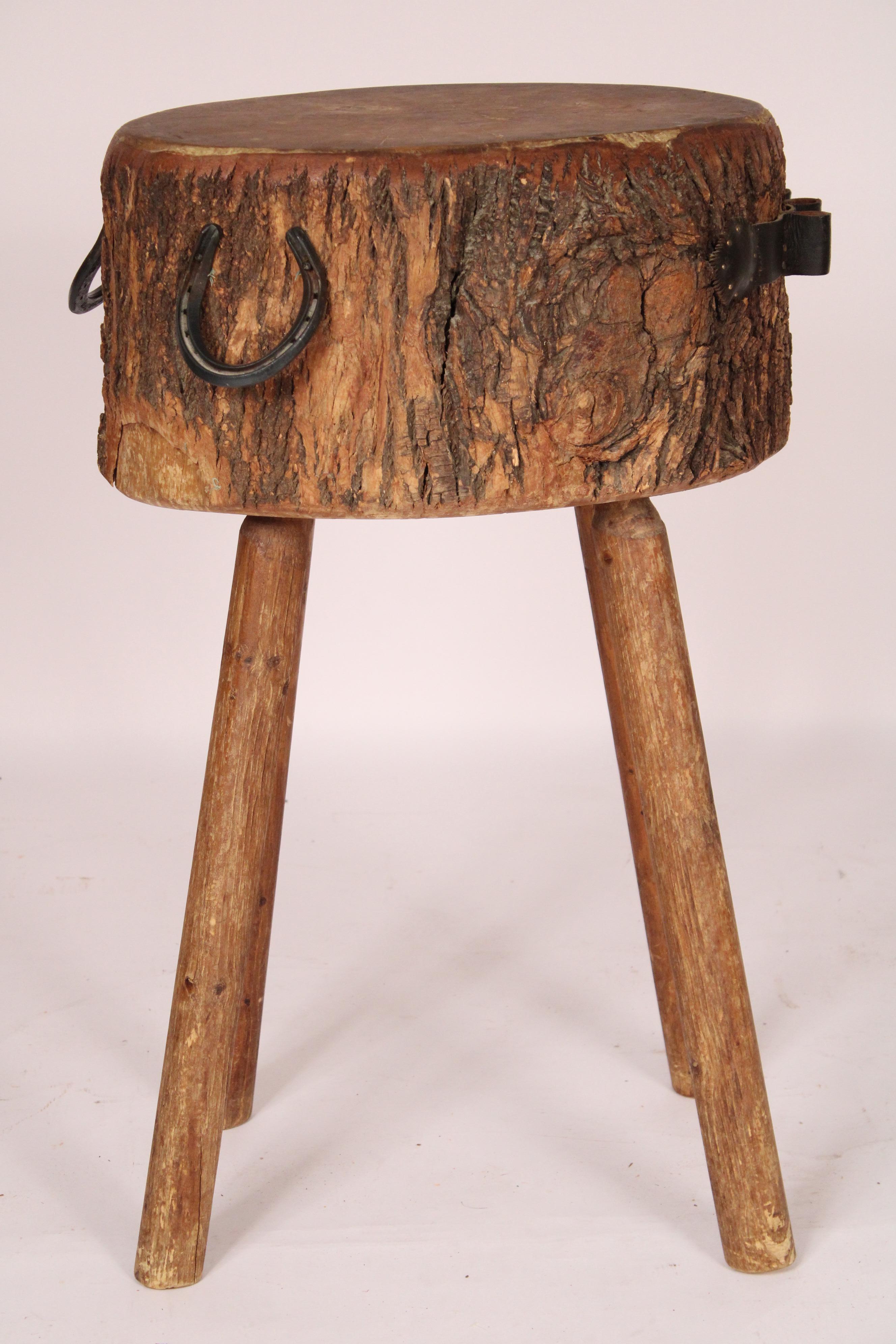 Vintage country butchers block table, circa mid 20th century. The top is a solid section of a tree trunk with two steel horseshoes handles and a leather cutlery holder, resting on turned legs.
