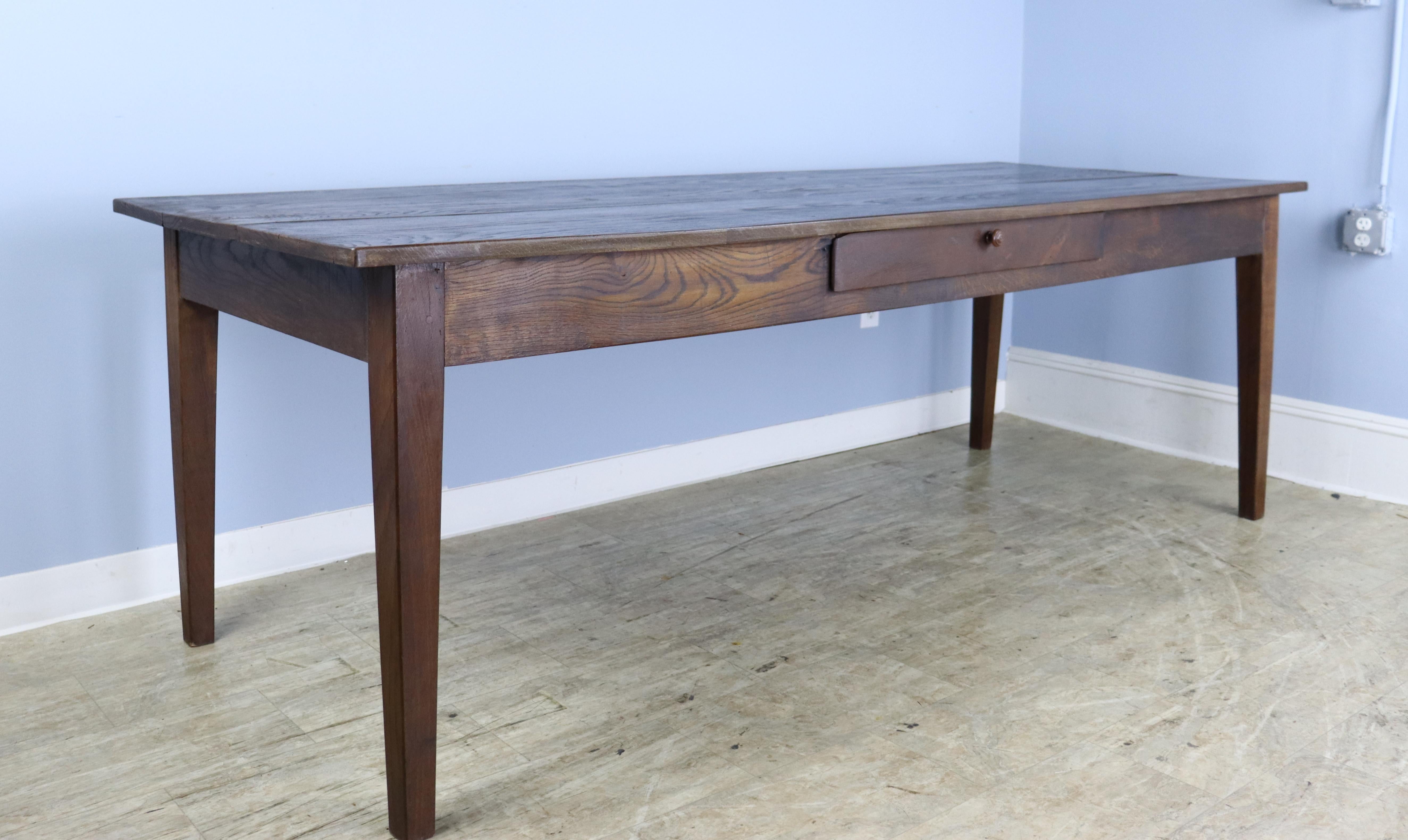 A long French chestnut farm table with a single center drawer.  Well grained top and classic tapered legs. 24.5 inch apron height is good for knees and there are 83 inches between the legs on the long side. The top has good color, grain and patina. 