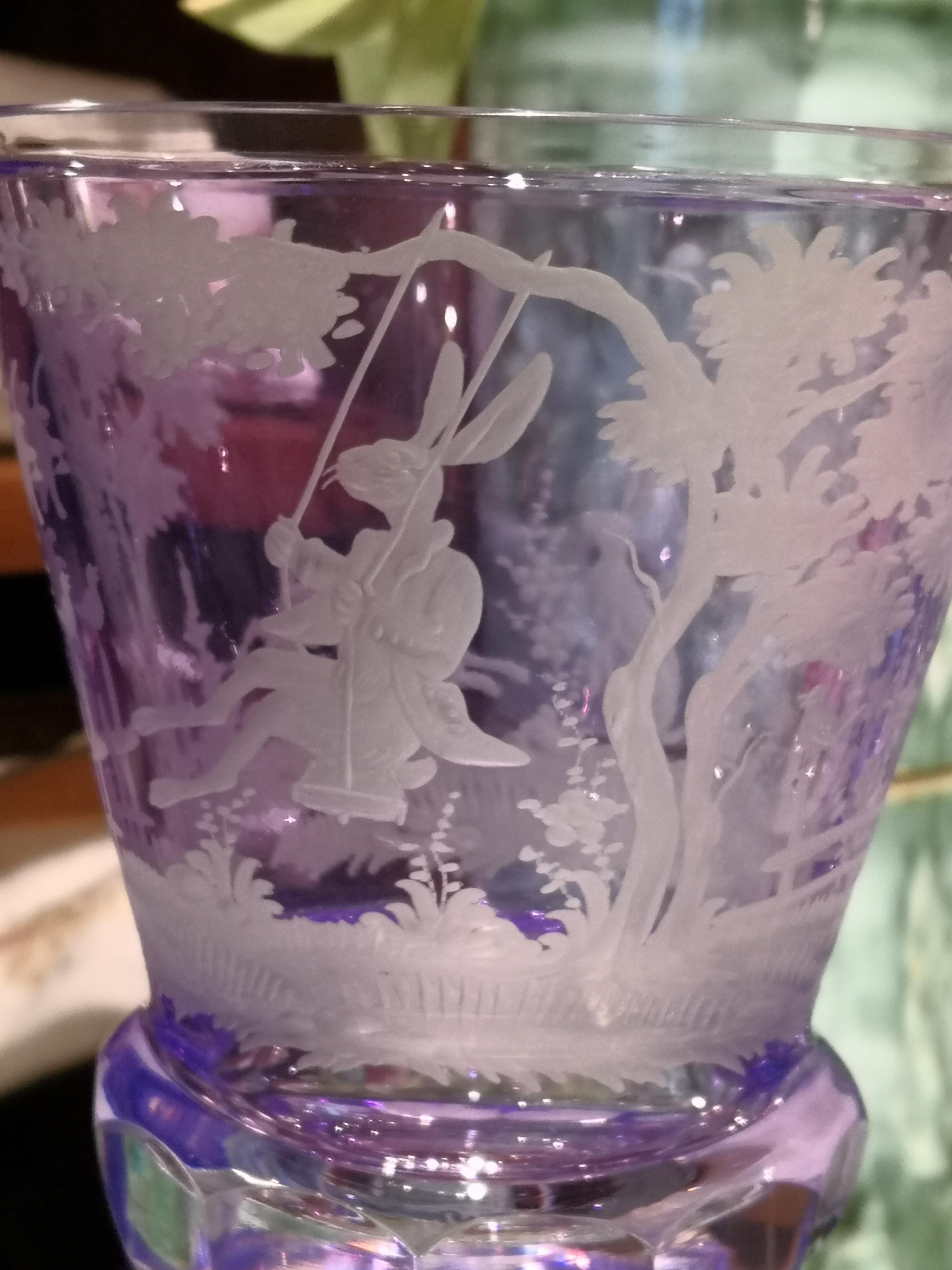 Hand blown crystal vase in purple with an antique country style Easter design. Hand carved by Bavarian glass artists . A rich garland of trees and flowers with rabitts all around. One rabbit sitting on a see-saw and two smaller rabbits decorate this