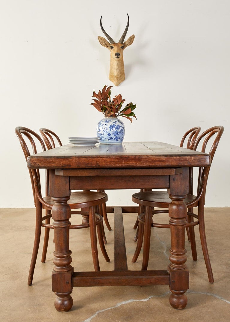 Rustic country English farmhouse dining table featuring a trestle style base. Crafted from oak with 2 inch thick plank top having bread board ends. Constructed with wood peg joinery. The top is supported by a trestle style base having a storage
