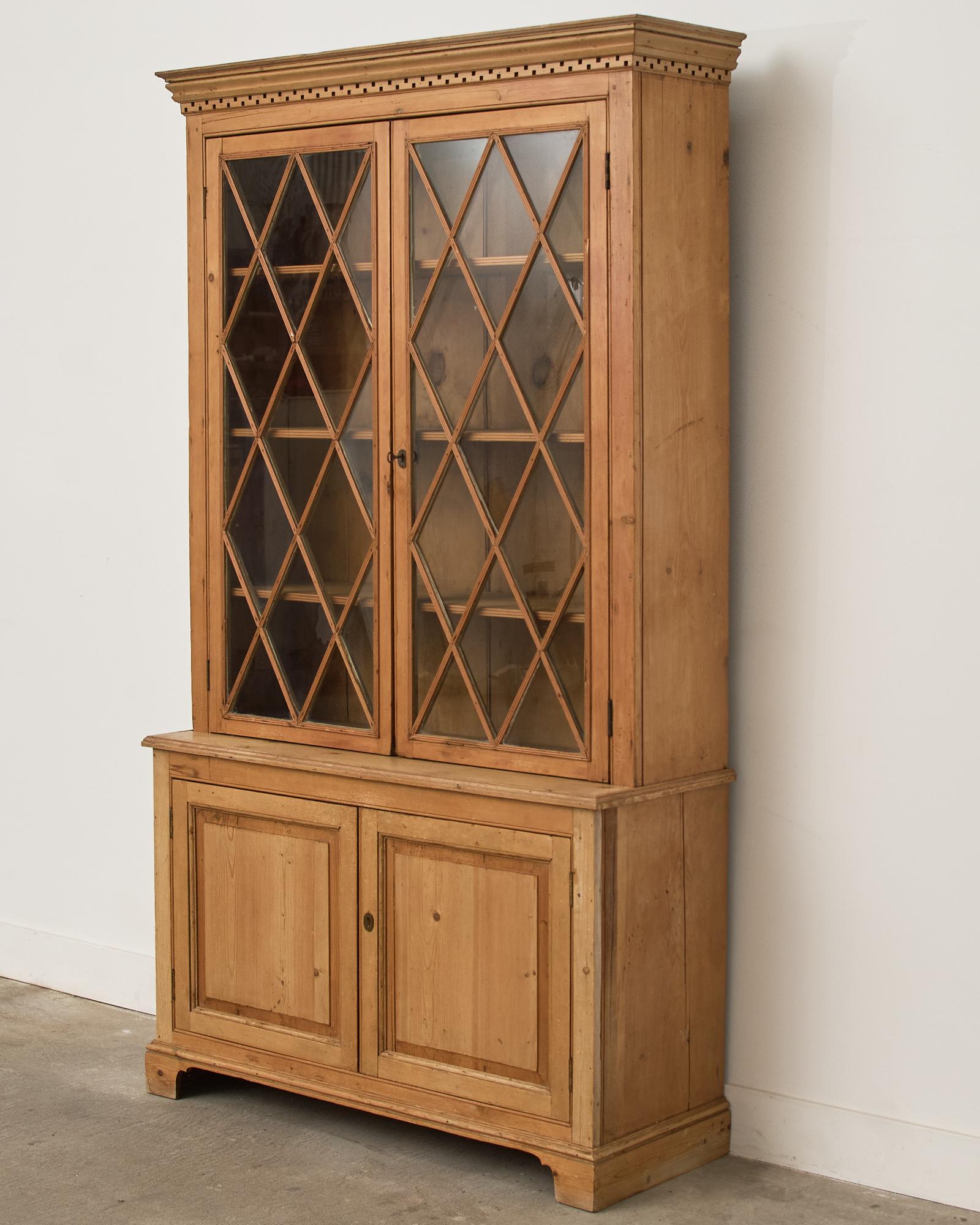 Gorgeous country English bookcase cabinet or cupboard made in the Georgian taste. The two-part cabinet is crafted from pine and has a step back top case. The top features an astragal glazed glass locking doors with a lattice design surmounted by a