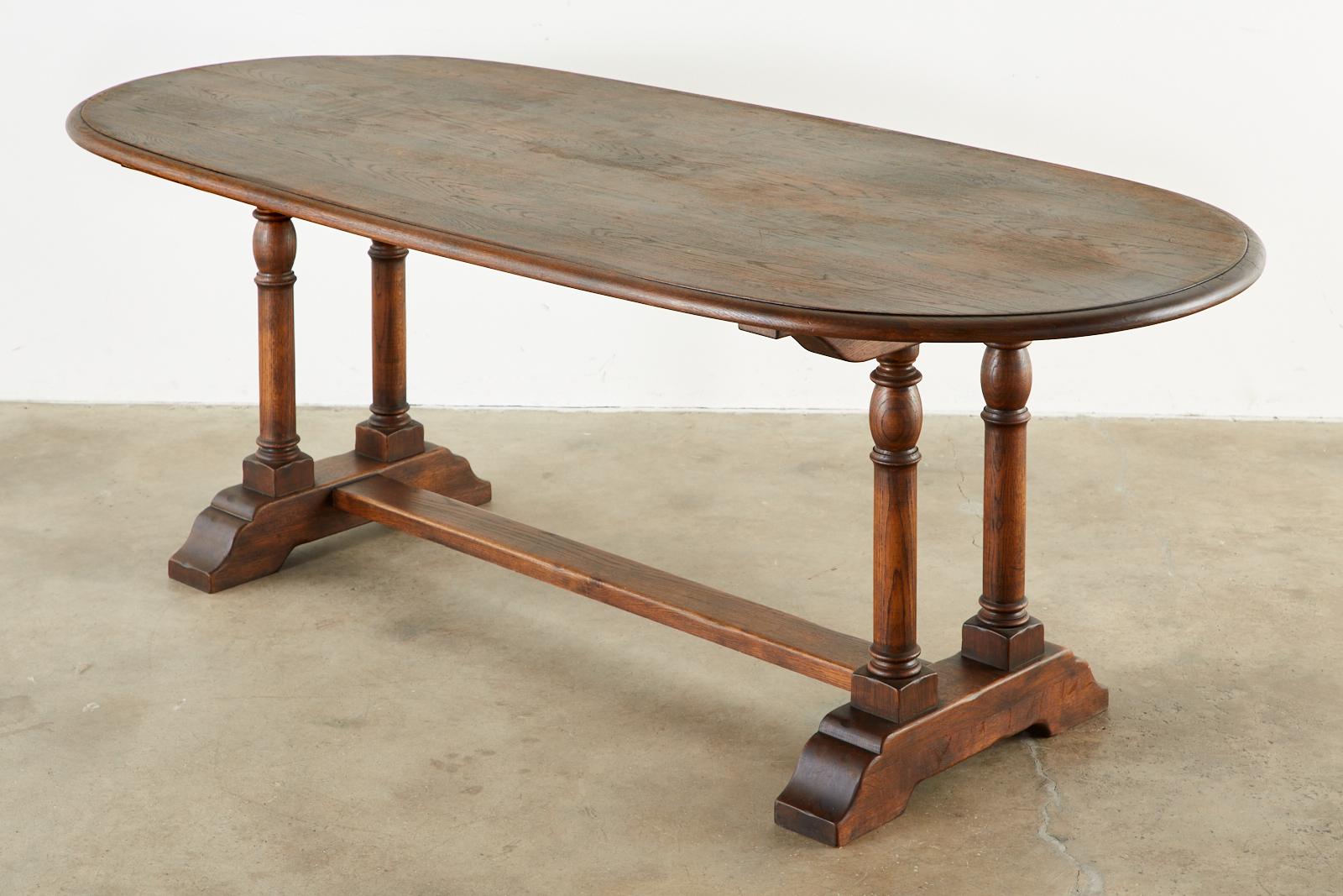 Handsome country English trestle dining table or library table featuring a thick, oval shaped plank top. Constructed from beautifully grained oak with a rich finish. The oval top has an ogee edge and is supported by a trestle base having pairs of