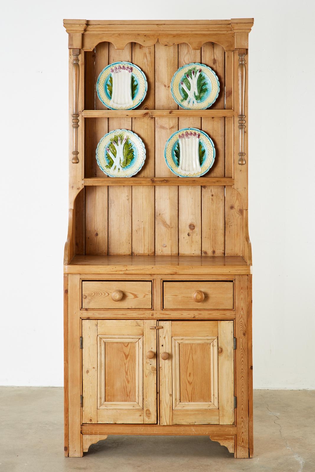 Rustic country English welsh dresser constructed from pine. The case features a two shelf cupboard on top decorated with pilaster columns on each side surmounted by a cornice top. The dresser is fronted by two storage drawers and two doors opening