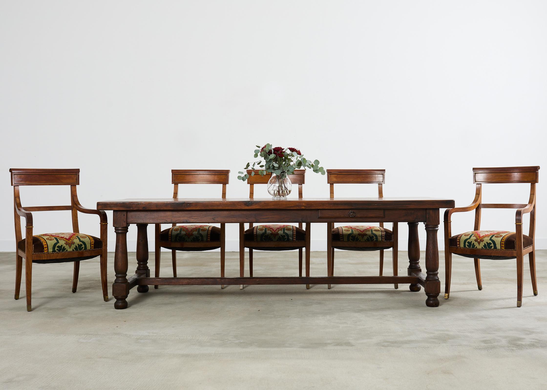 Rustic country English provincial style farmhouse dining table crafted from solid oak. The table features a 2.5 inch thick top of oak timbers showcasing amazing woodgrain patterns and knots. The top is supported by a large trestle base with turned