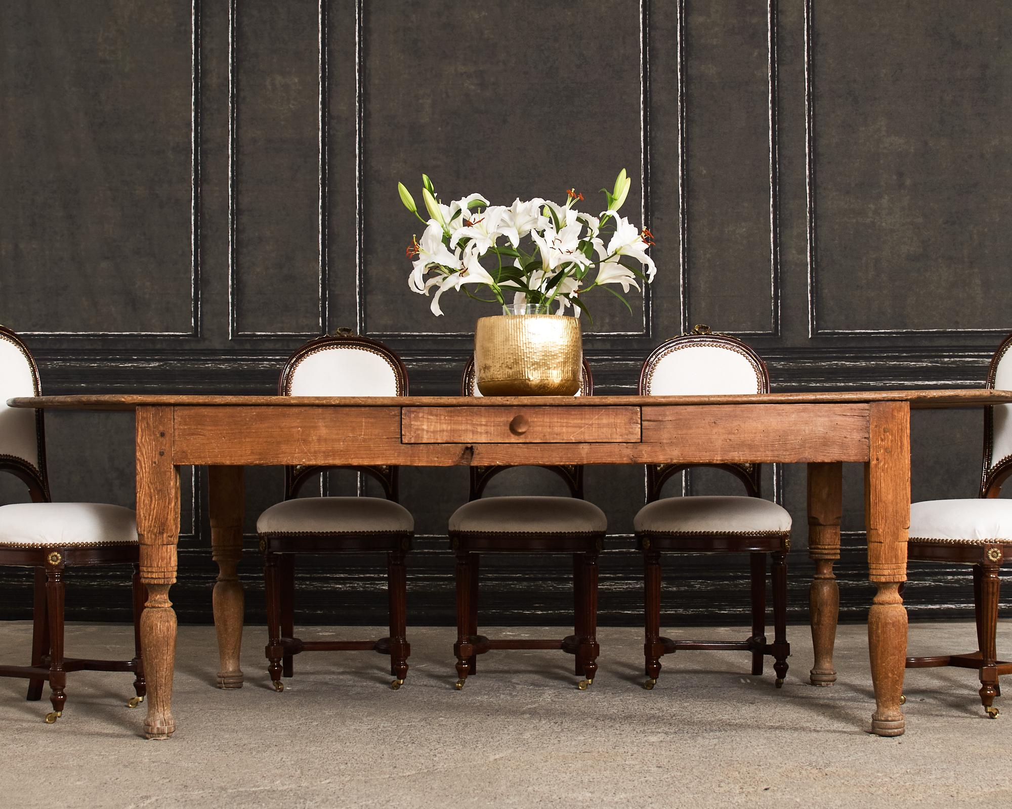 Weathered late 19th century country English provincial oval farmhouse dining table crafted from pine. The table features an oval top constructed with thick planks. The base has wood peg joinery with a small storage drawer on one side of the apron.
