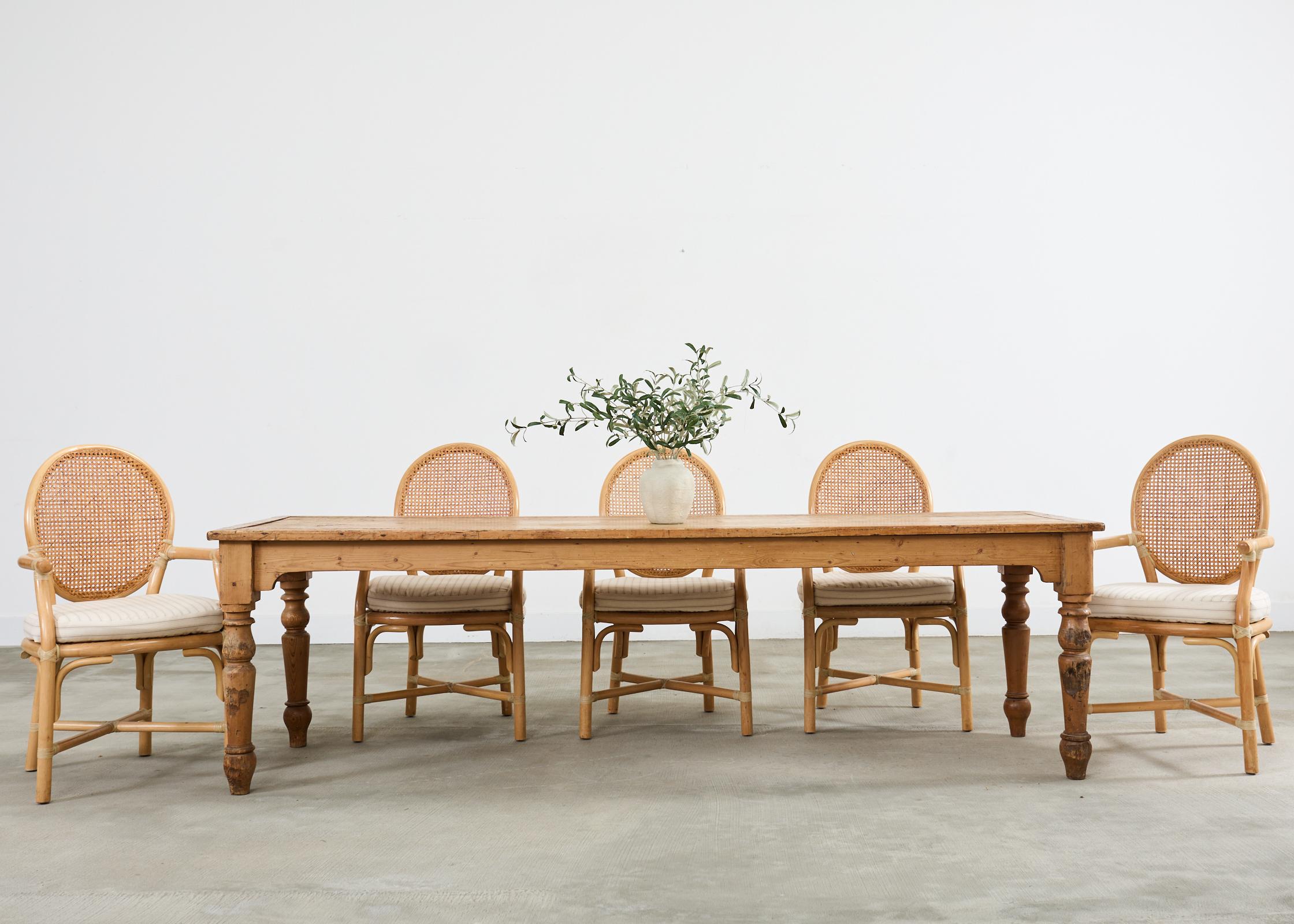 Rustic and weathered country English provincial farmhouse harvest dining table crafted from pine. The grand table measures over 8 feet long and features a 1 inch thick framed top constructed from planks. The apron has gracefully shaped sides that