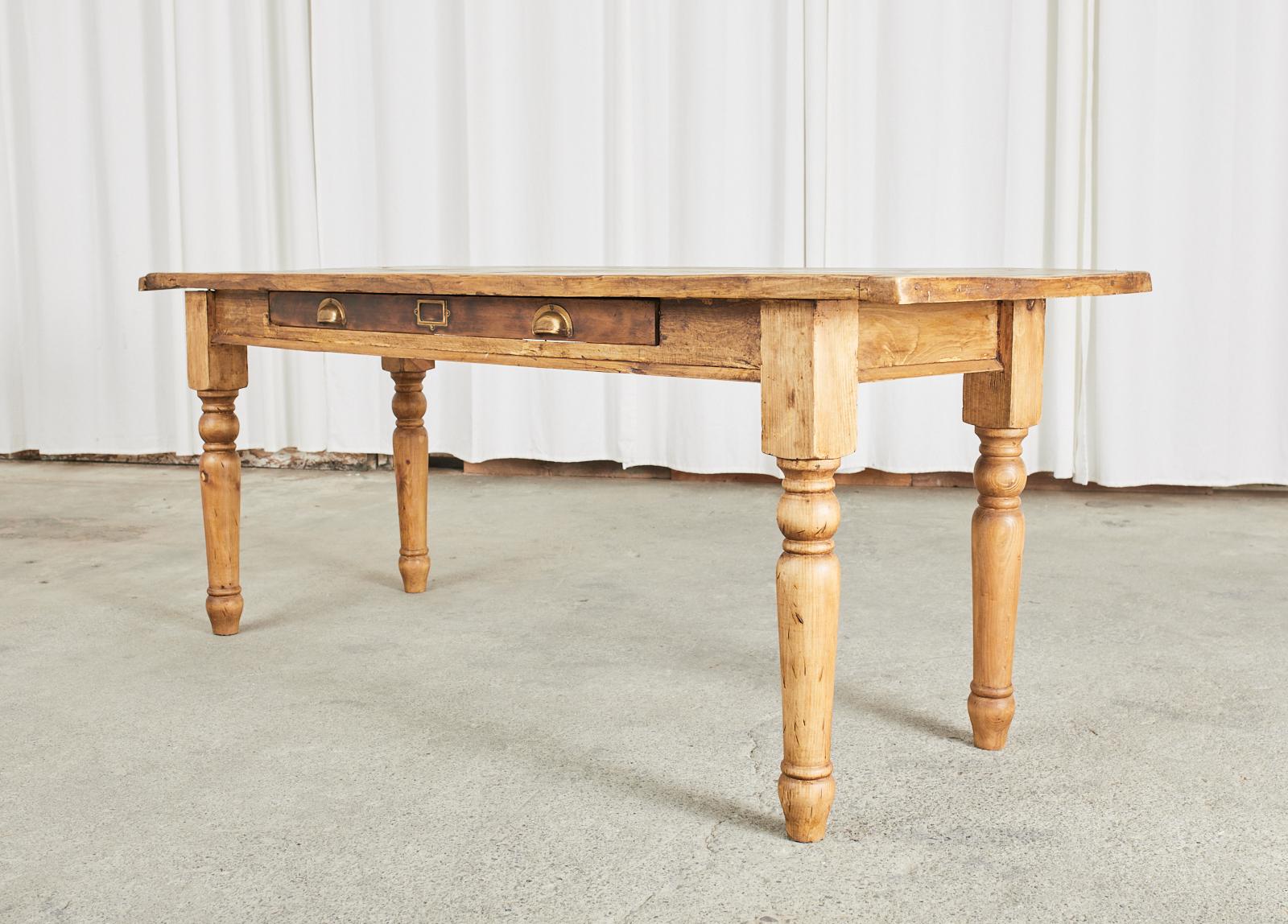 Rustic country English farmhouse dining table or harvest table that could also serve as a console, desk, or writing table. The table features a 1 inch thick plank top with breadboard ends. There is a large storage drawer on the front frieze with a
