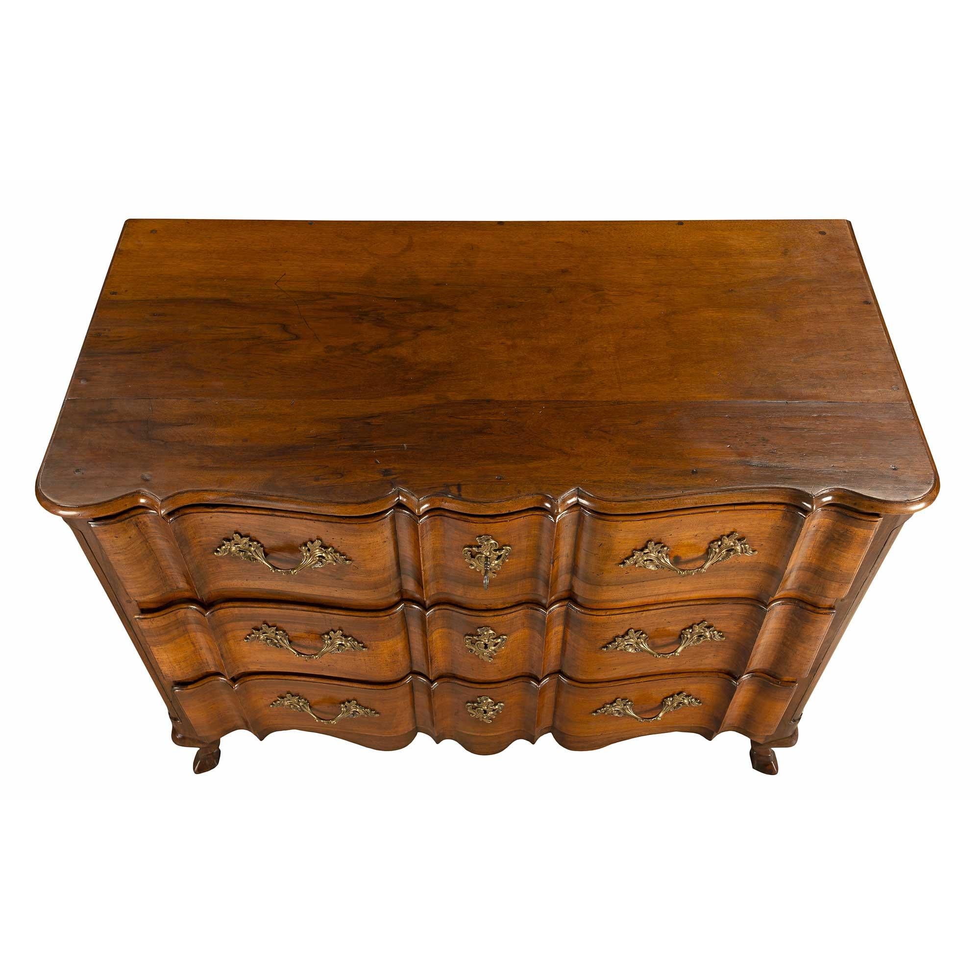 A handsome and most elegant Country French 18th century walnut three-drawer commode. The chest is raised by fine scrolled legs with carved hoof feet. Above the beautiful scallop-shaped frieze are three drawers with a most decorative and unique shape