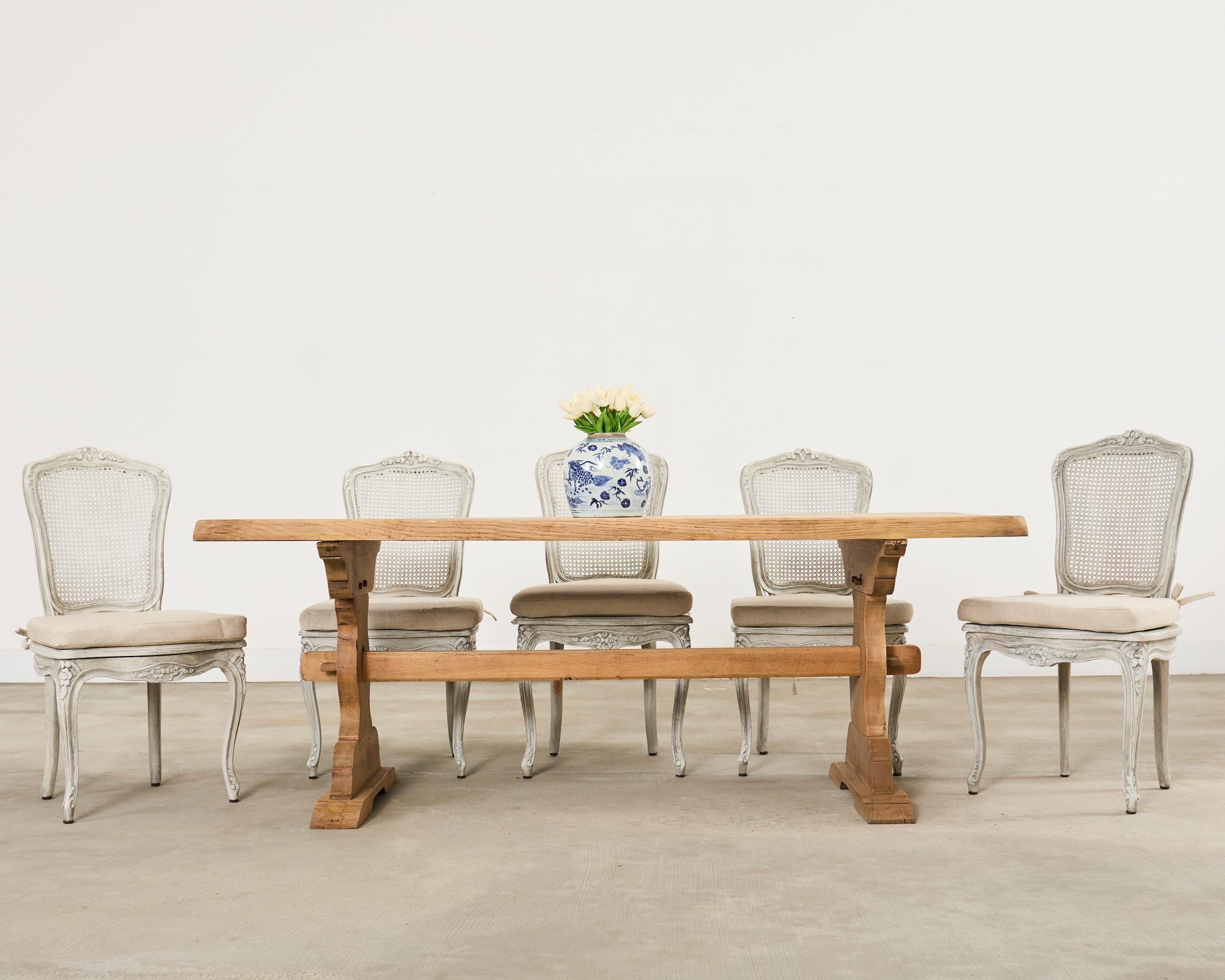 Mesa de comedor rústica de estilo provinciano francés del siglo XX con acabado de roble blanqueado. La mesa tiene un tablero de 2 pulgadas de grosor apoyado en una base de caballete. Las patas, en forma de reloj de arena, están unidas por un largo