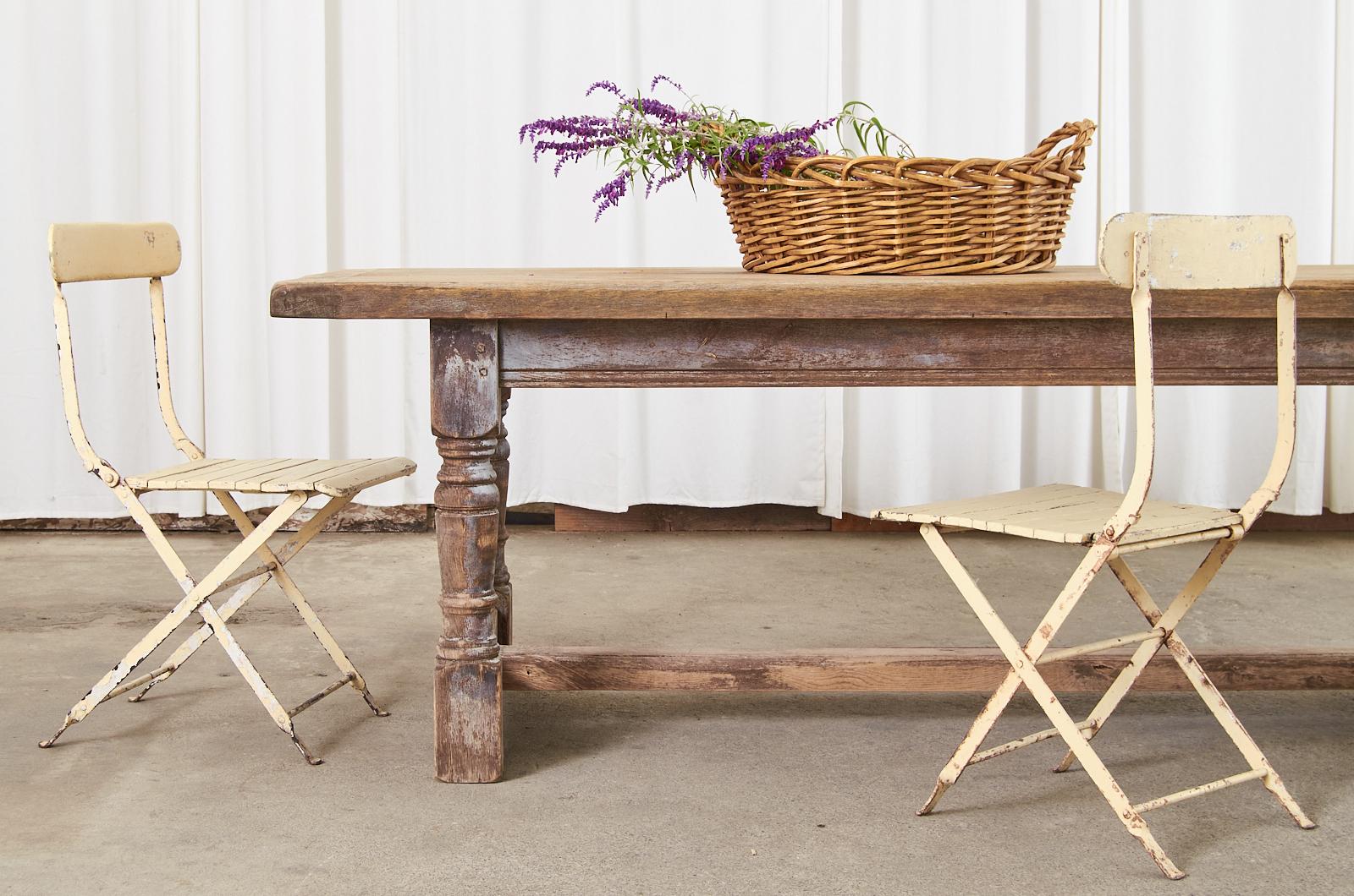 Massive rustic country French farmhouse trestle dining table featuring a beautifully distressed bleached oak finish and patina. The top is crafted from 2 inch thick solid oak planks with breadboard ends and hand-forged iron bolts on the ends. The