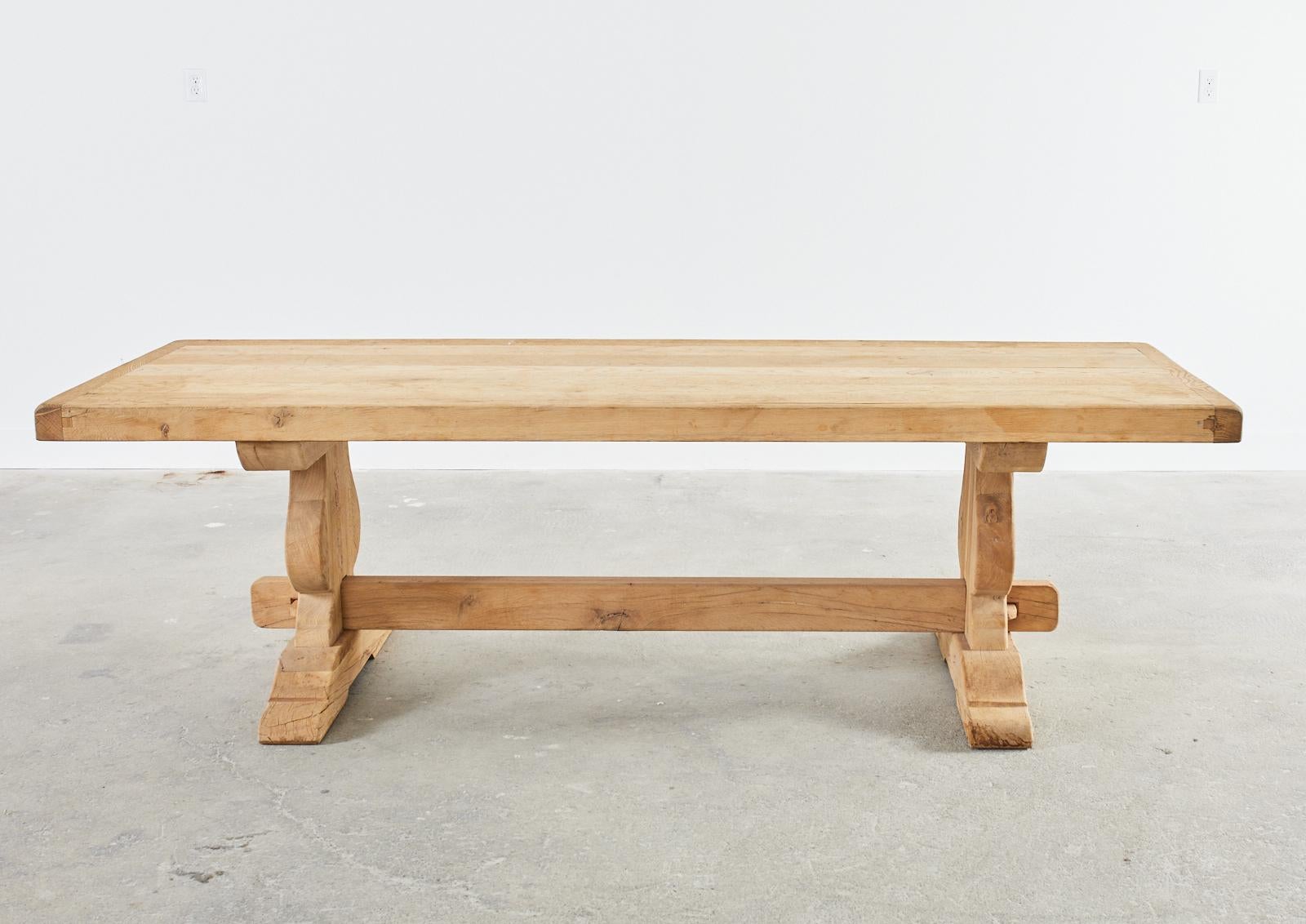 Massive country French provincial style farmhouse trestle dining table or harvest table. Hand-crafted from solid oak having a 3-inch thick plank top with breadboard ends. The trestle style base has spade shaped legs ending with 5 inch thick feet.