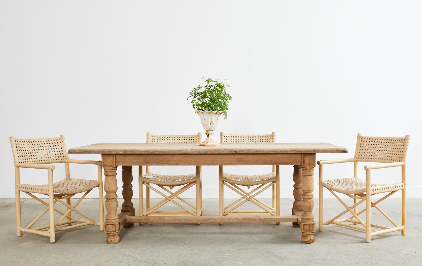 Rustic Country French farmhouse dining table featuring a weathered bleached oak finish with an amazing aged patina. Constructed with a 1.5-inch thick plank top supported by a trestle-style base. The turned legs are thick with chunky block joints